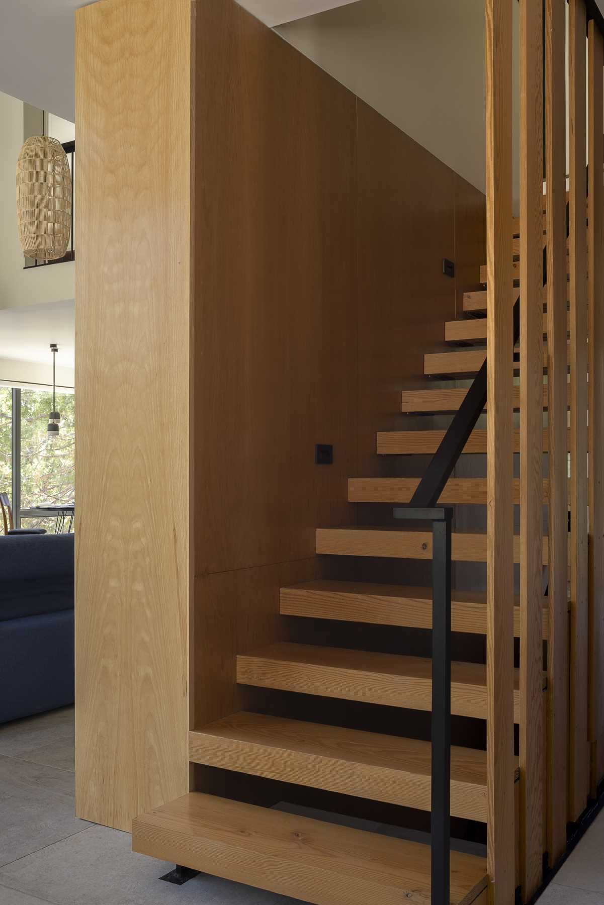 The main floor stair treads are fashioned from thick pieces of reclaimed fir and give the impression of a floating staircase; however, they are cleverly supported by a series of overlapping slats that echo the vertical layout of the exterior siding and the surrounding trees.