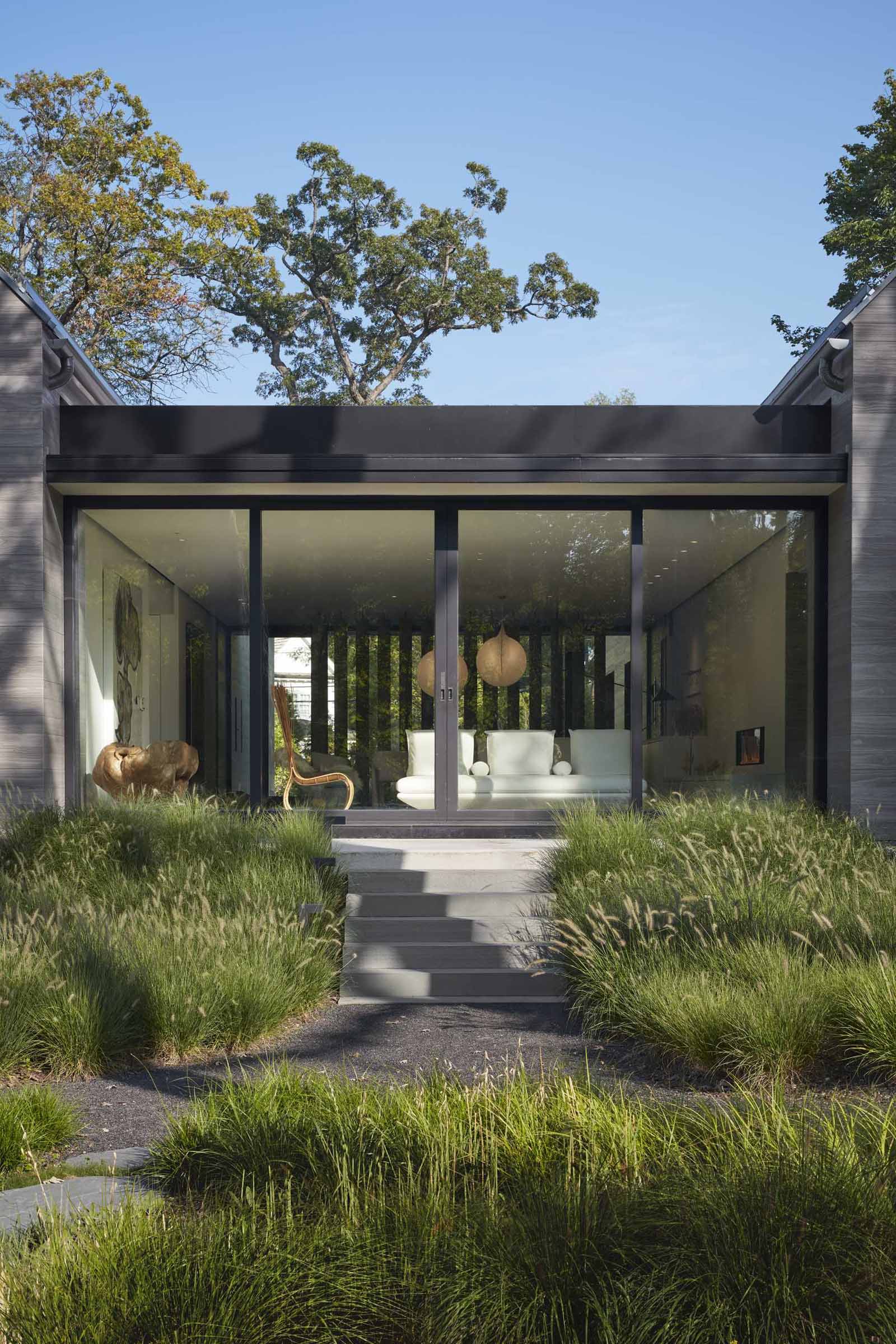 Sliding glass doors open the breezeway of this modern house to outdoor stairs flanked by various grasses.