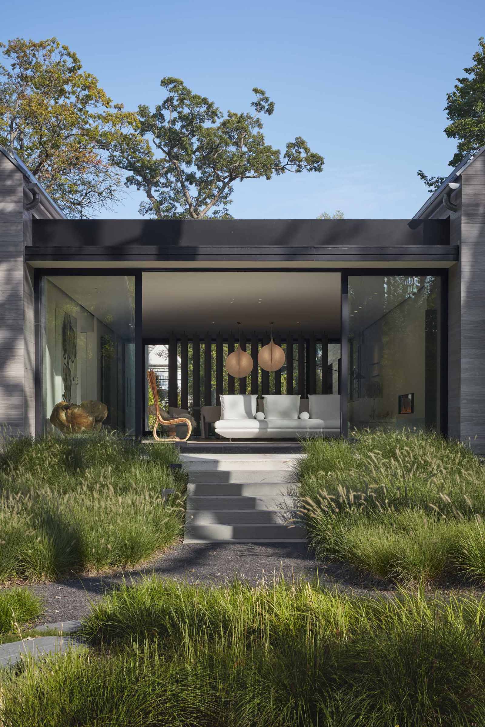 Sliding glass doors open the breezeway of this modern house to outdoor stairs flanked by various grasses.