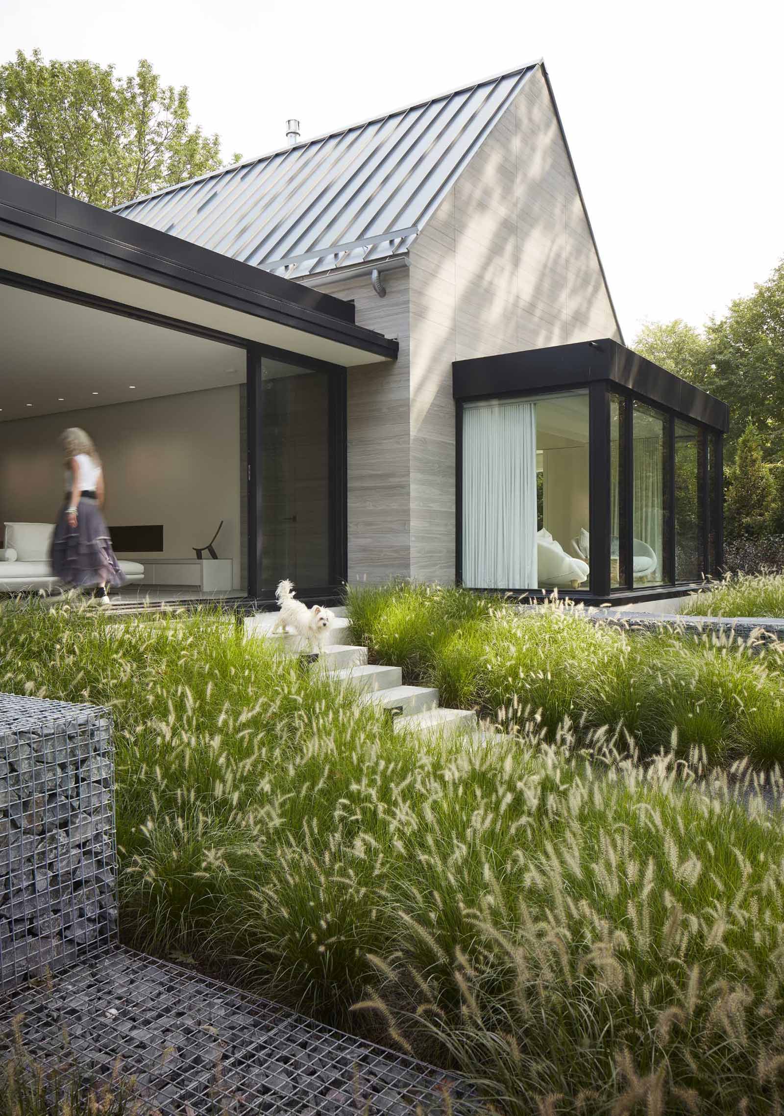 Sliding glass doors open the breezeway of this modern house to outdoor stairs flanked by various grasses.