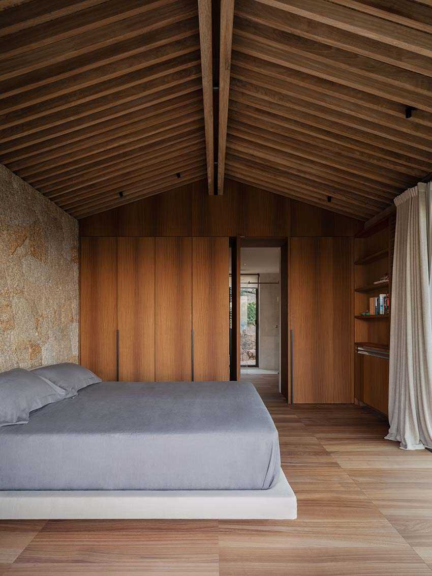 In the bedroom, the granite walls provide a backdrop for the bed, while Iroko wood was used to create the built-in wardrobe.