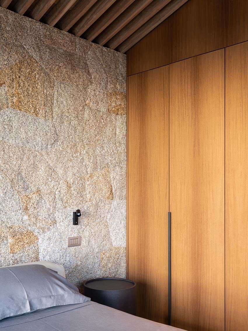 In the bedroom, the granite walls provide a backdrop for the bed, while Iroko wood was used to create the built-in wardrobe.