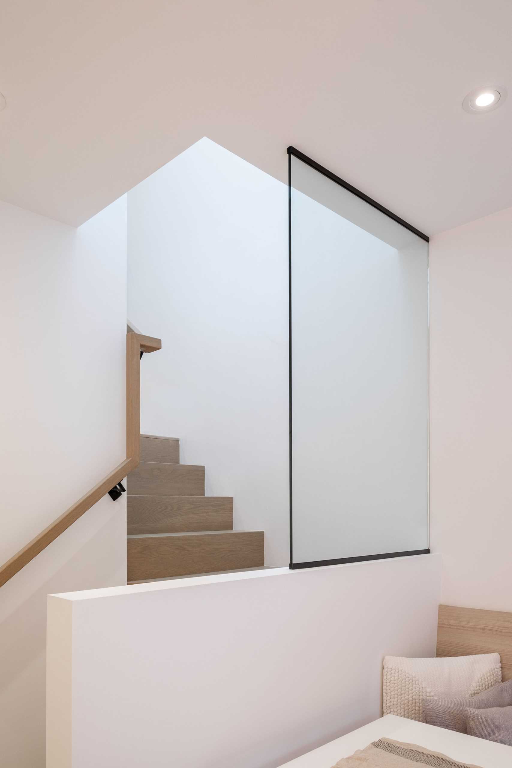 Stairs between the den and the dining area/kitchen, lead to the upper level of this laneway home, while a glass partition and railing allows natural light to travel throughout the interior.