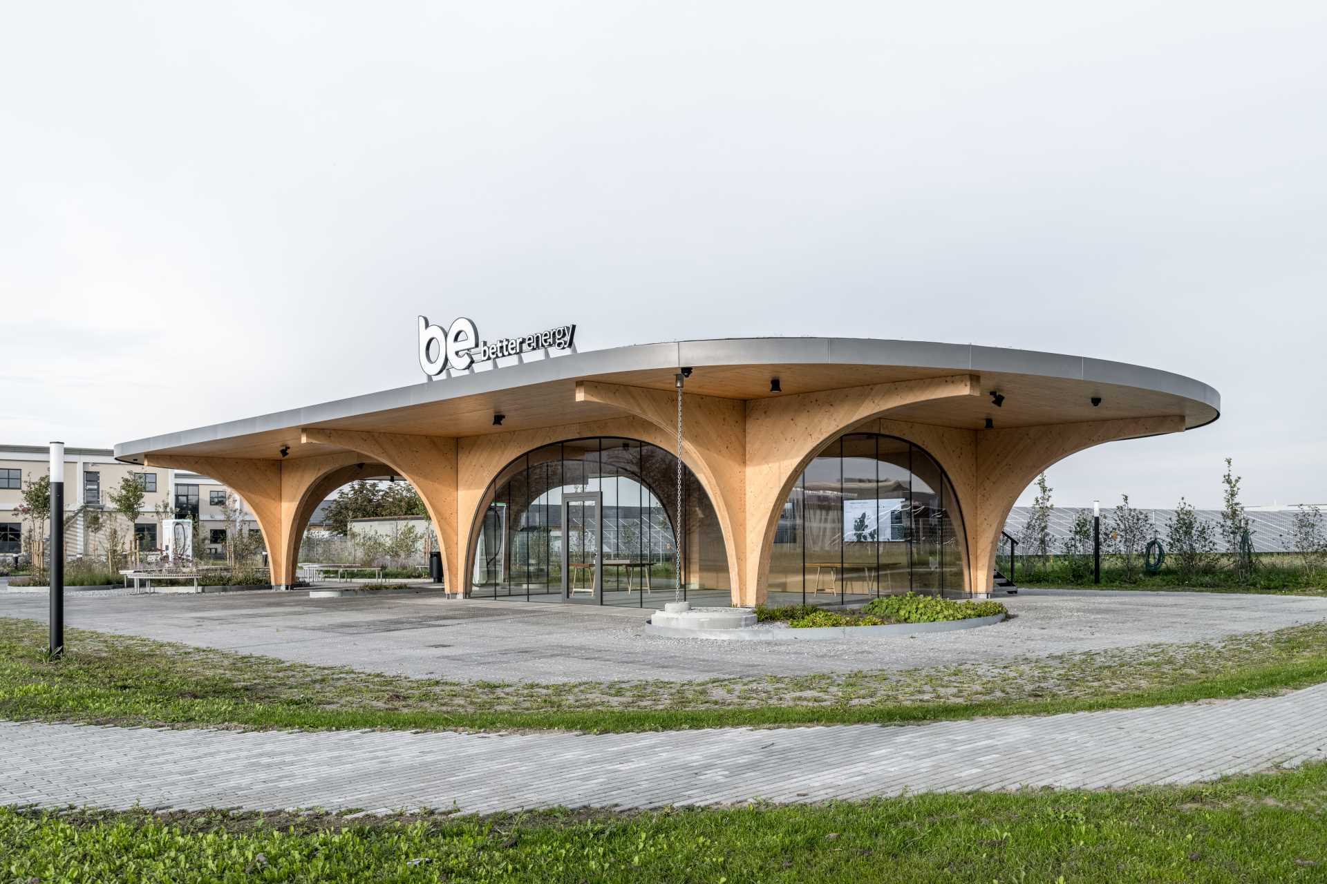 A contemporary charging park features an exposed wood structure and a park with native plants.