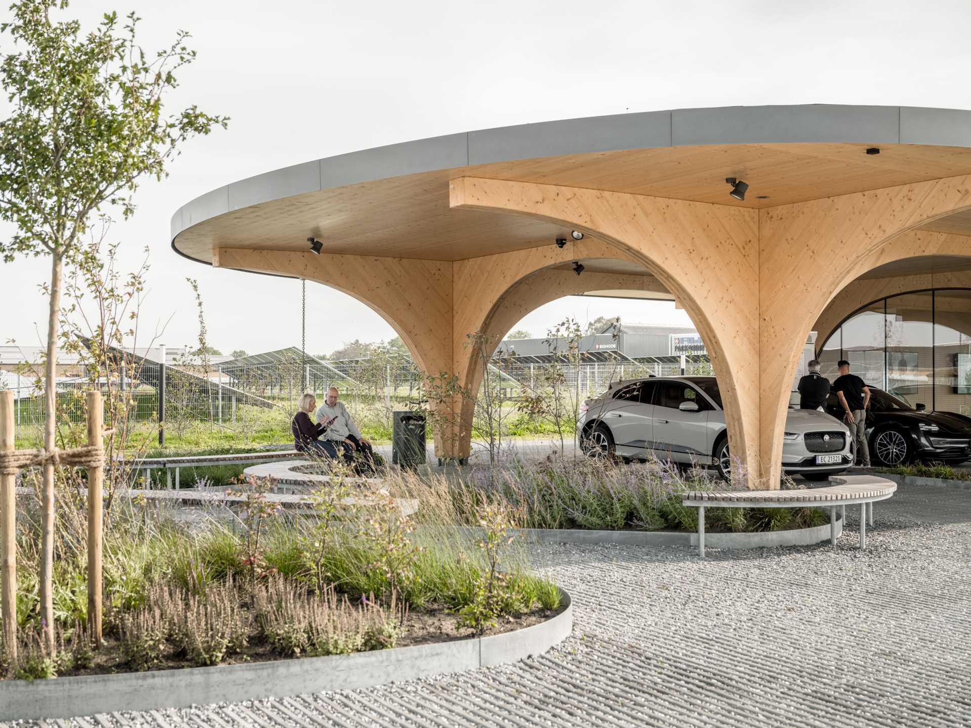 A contemporary charging park features an exposed wood structure and a park with native plants.