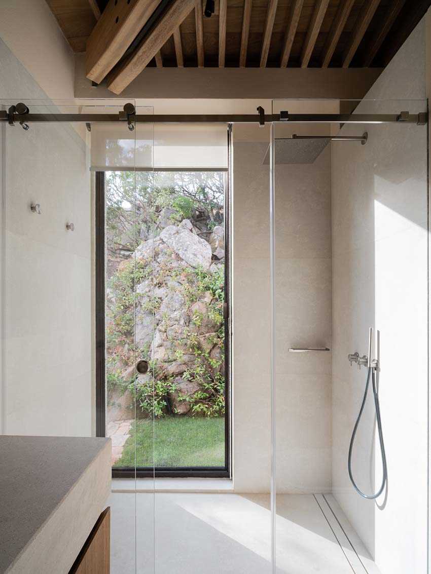 In this bathroom, a tall window is featured in the s،wer, providing natural light and a view of the garden.