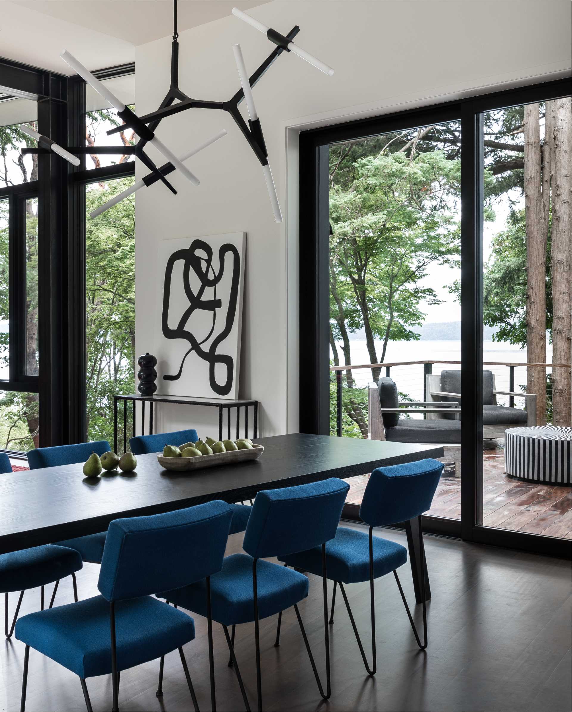 В этой современной столовой скульптурный светильник висит над длинным обеденным столом, а синие обеденные стулья дополняют мебель в гостиной.
