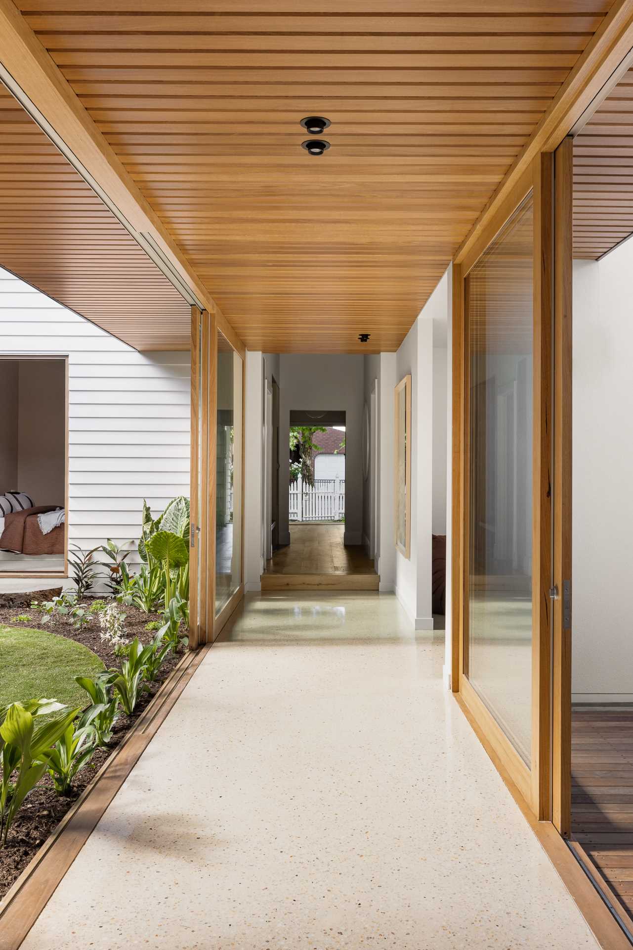 The hallway transitions into a walkway with sliding glass doors that connect to the outdoor spaces on each site.