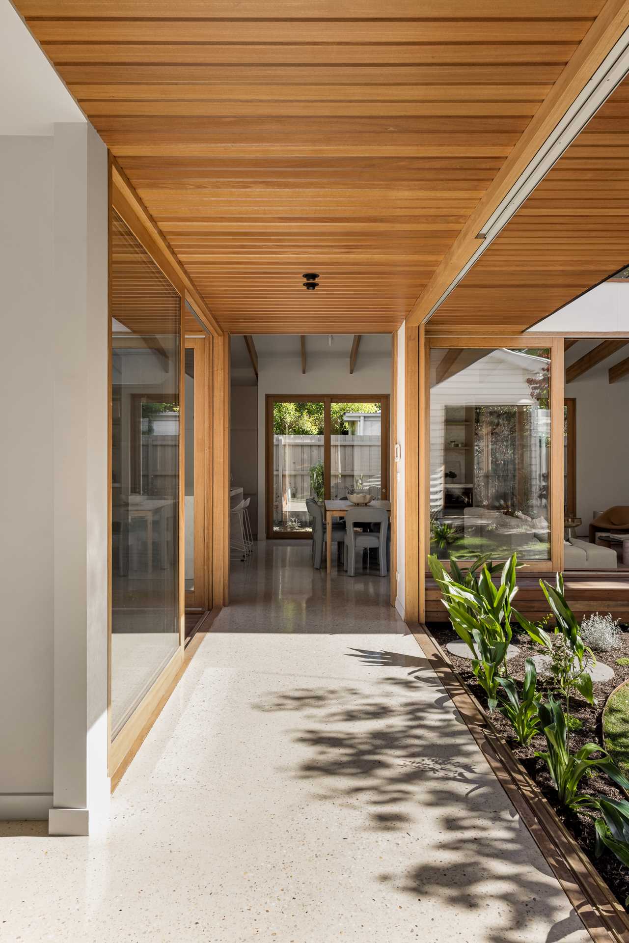 The hallway transitions into a walkway with sliding glass doors that connect to the outdoor spaces on each site.