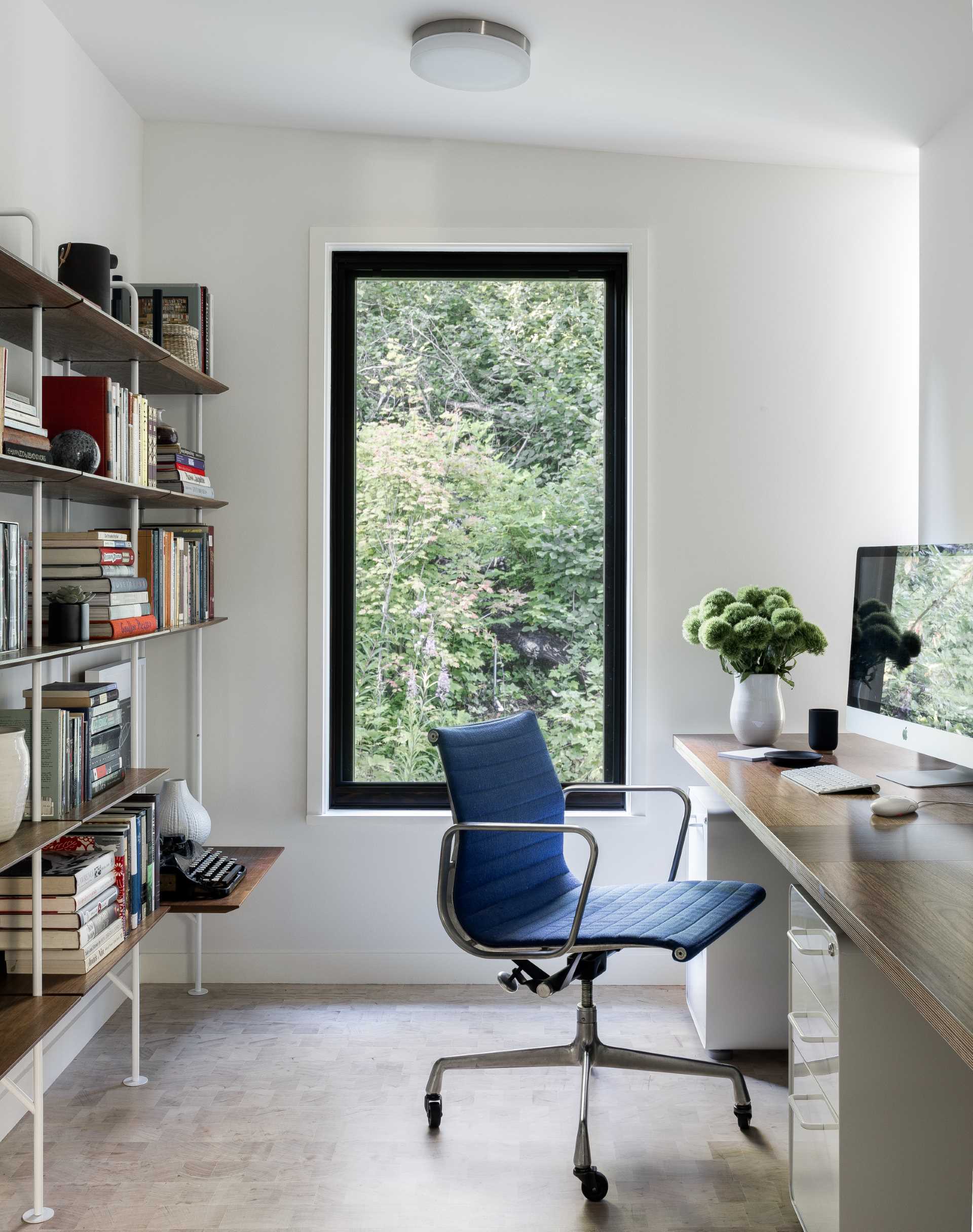 A home office furnished with a shelving unit and a desk, enjoys natural light from the vertical window.