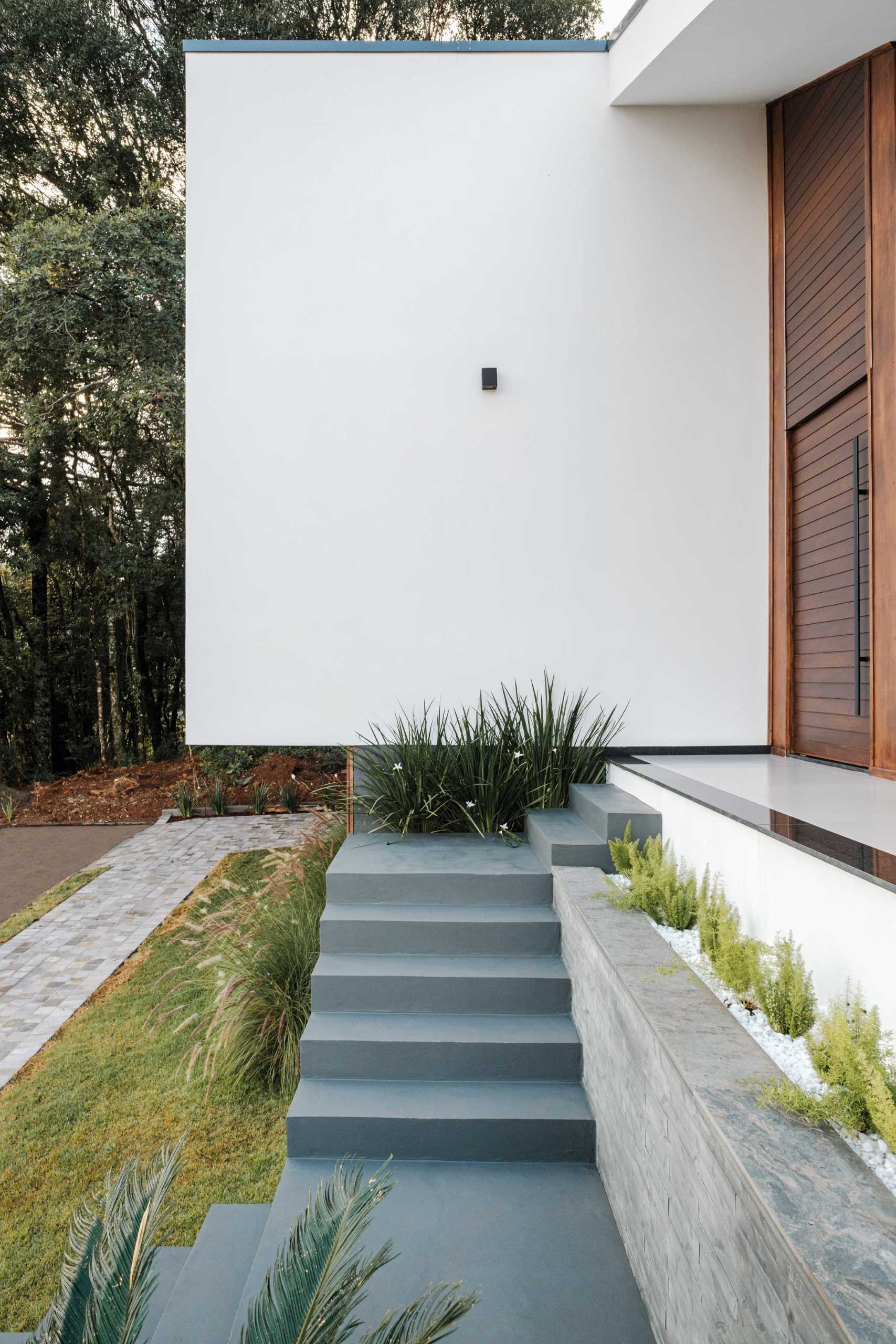 Современный дом со ступеньками, ведущими через ландшафтный дизайн и встроенные цветочные горшки к входной двери.
