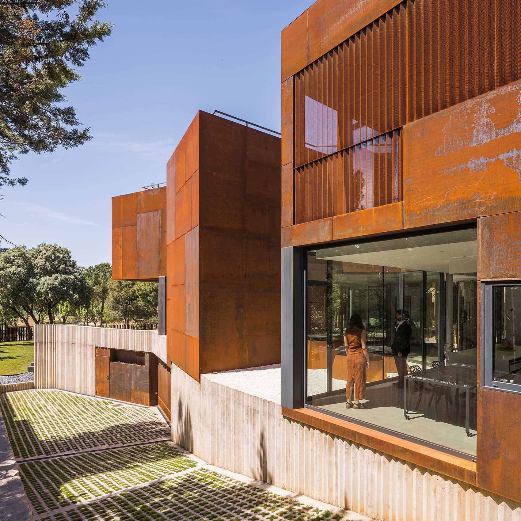 A modern house features large windows, cantilevered elements, and a weathered steel facade.