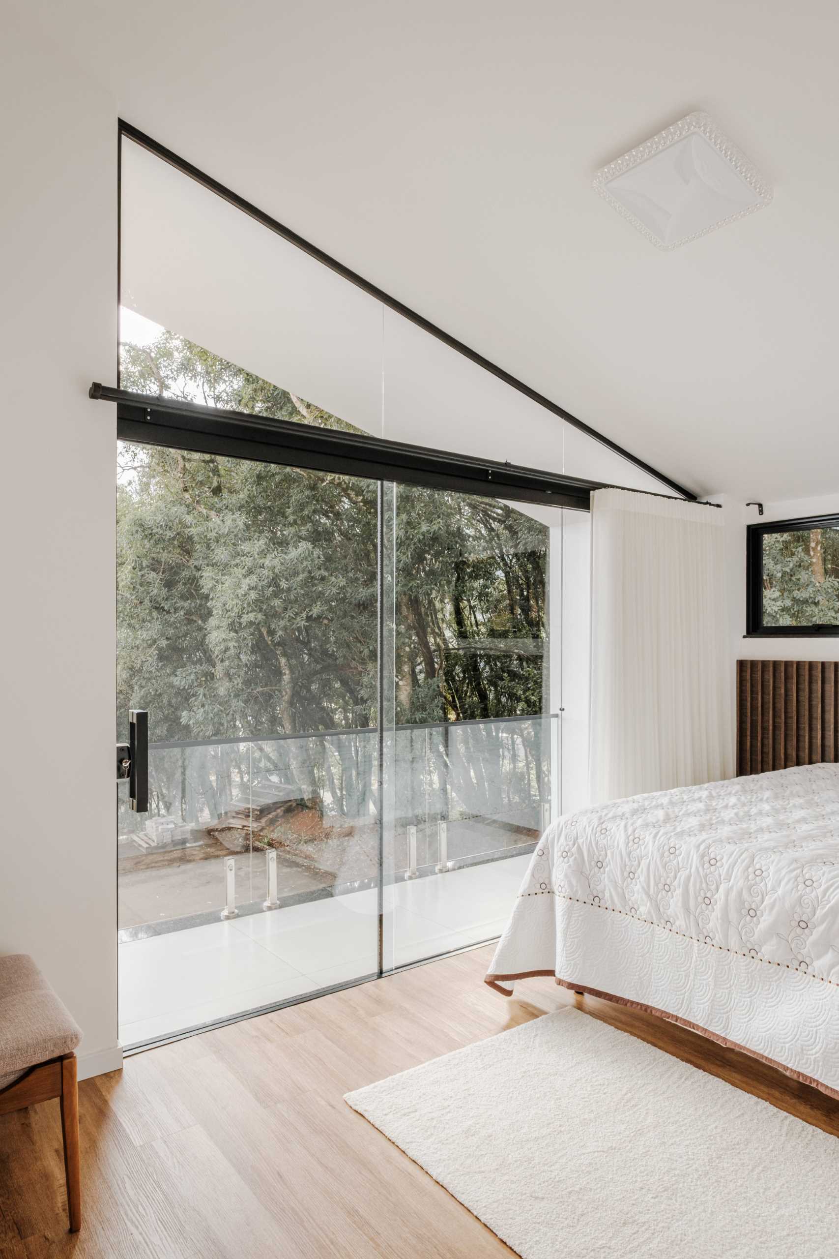 In this modern bedroom, the window follows the angled roofline, and a sliding door connects the space with the balcony.
