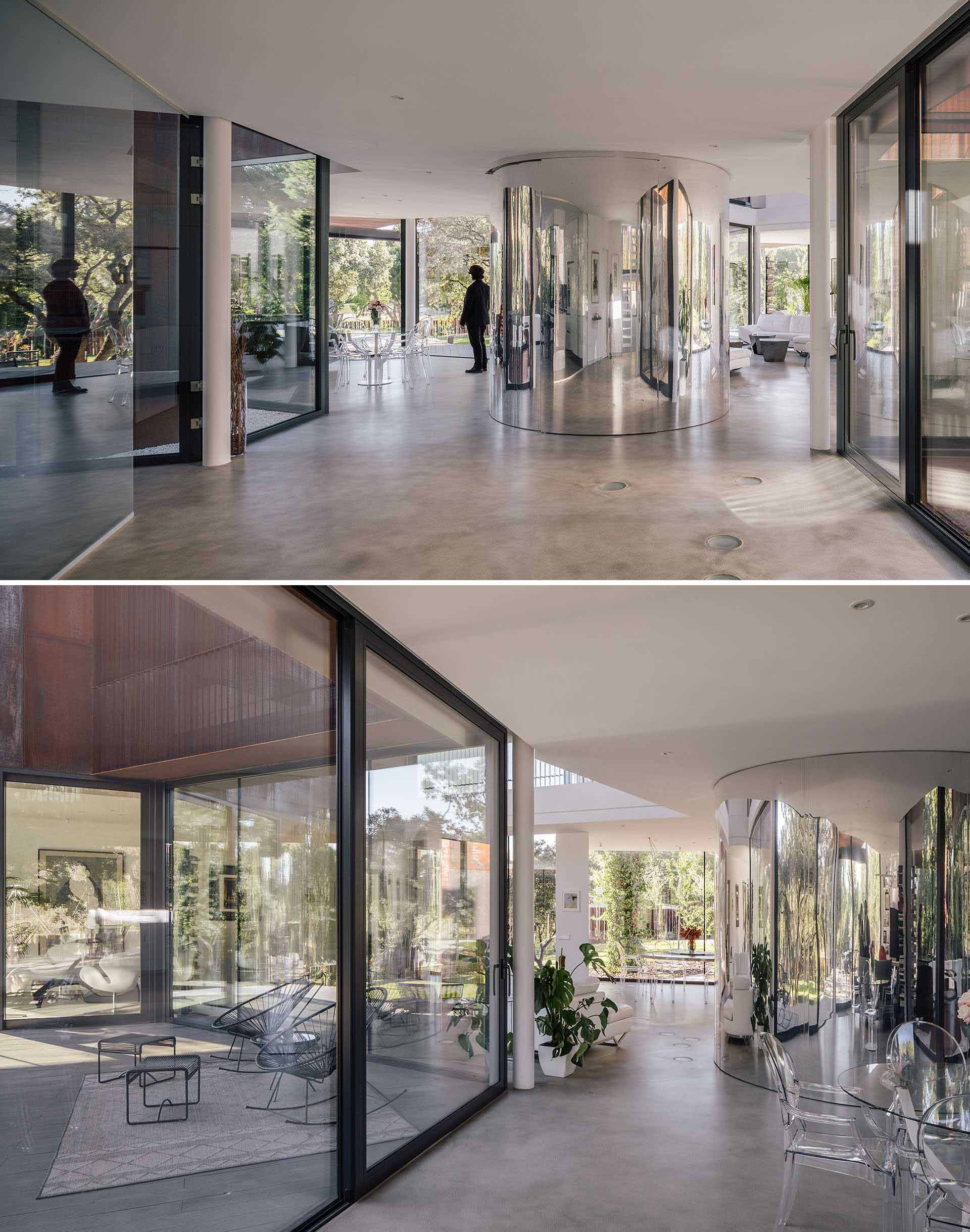 The interior of the home includes concrete floors, walls of glass, and a curved mirrored accent wall that reflects its surroundings.