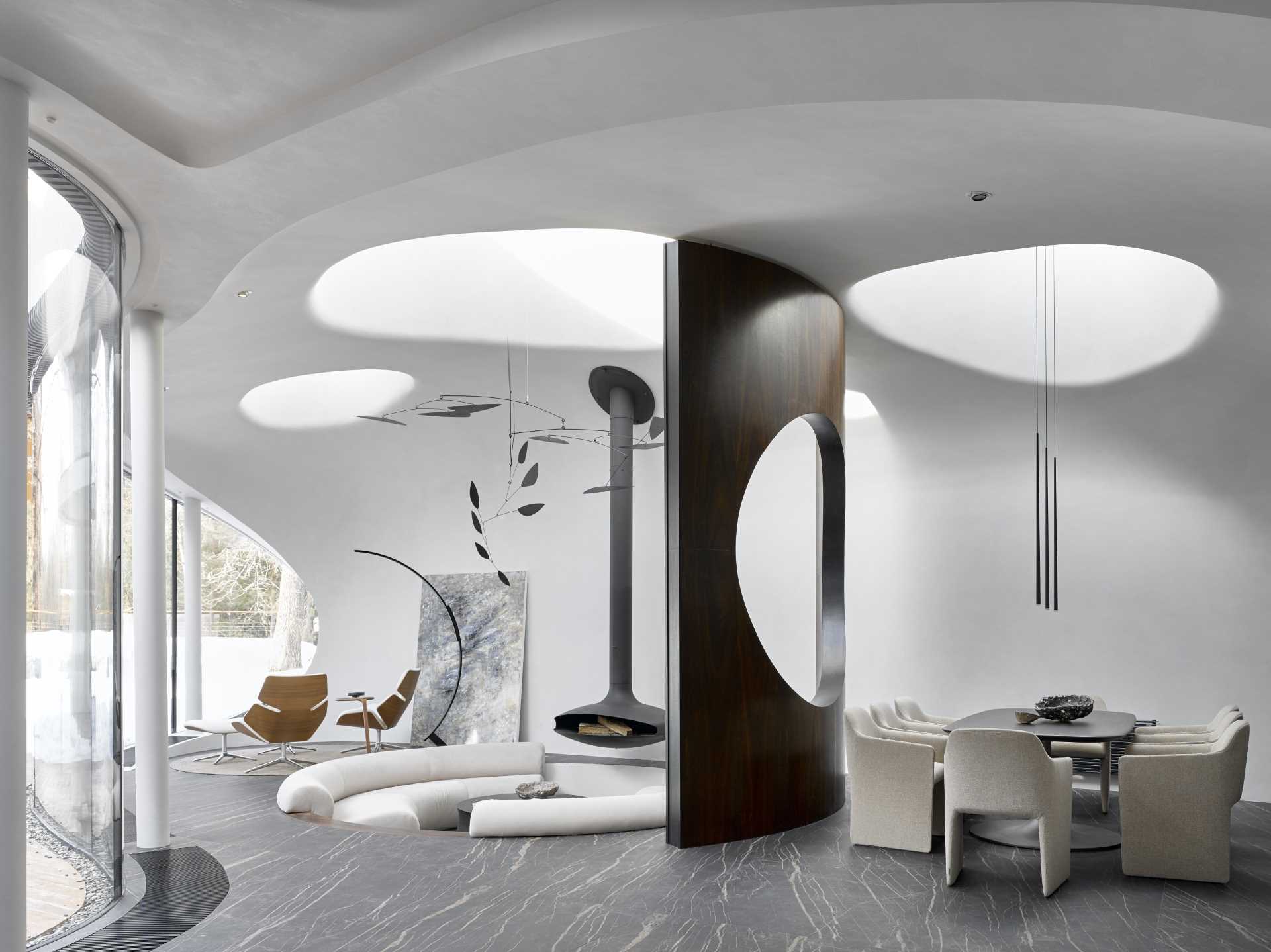 The organic shapes of this modern house continue through to the interior, with skylights, and a round sunken living room with a hanging fireplace. A curved partition wall with a round opening separates the dining room from the living room.