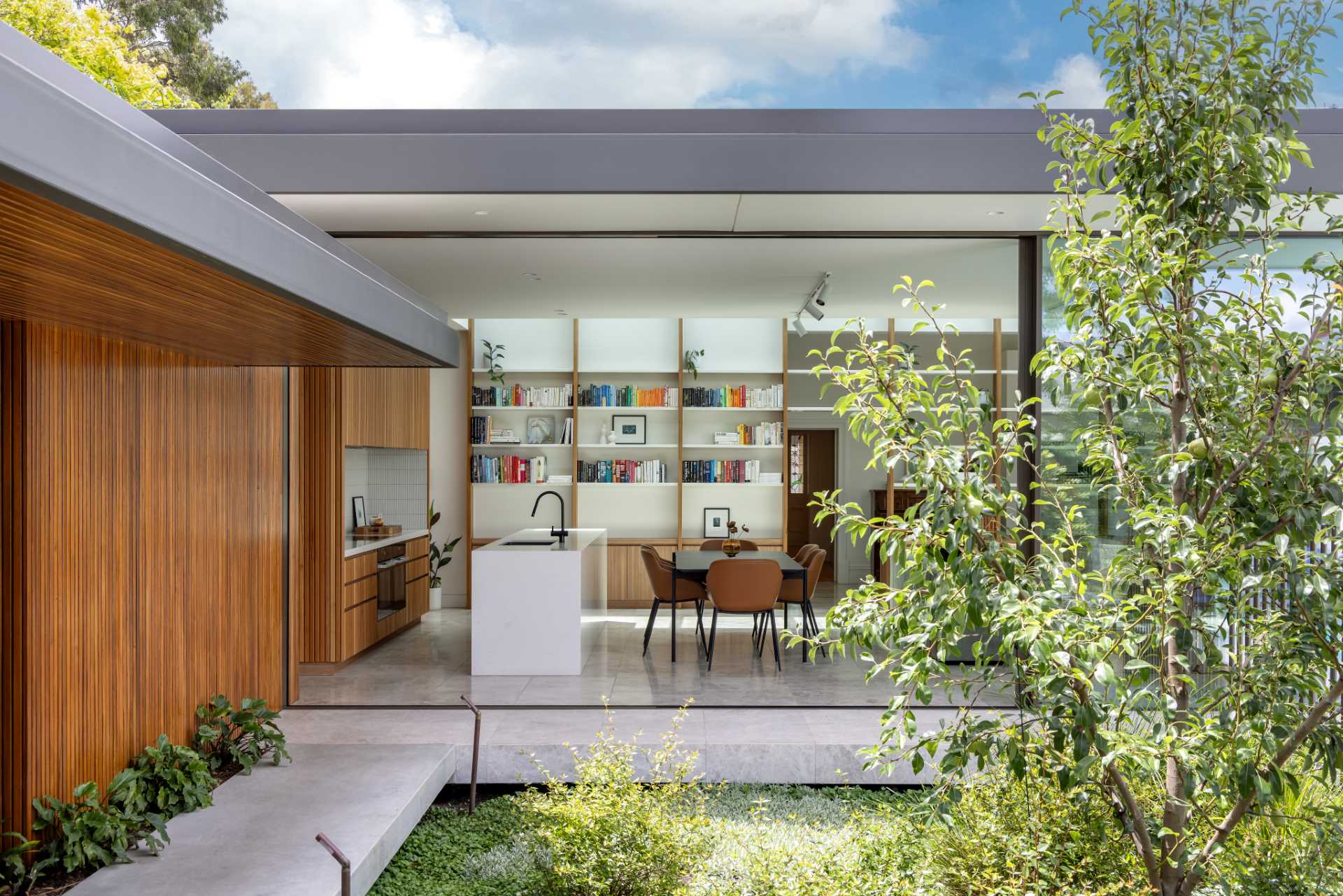 A modern kitchen features wood cabinets, Japanese ceramic tiles, laid vertically as a backsplash, and a minimalist stone island.