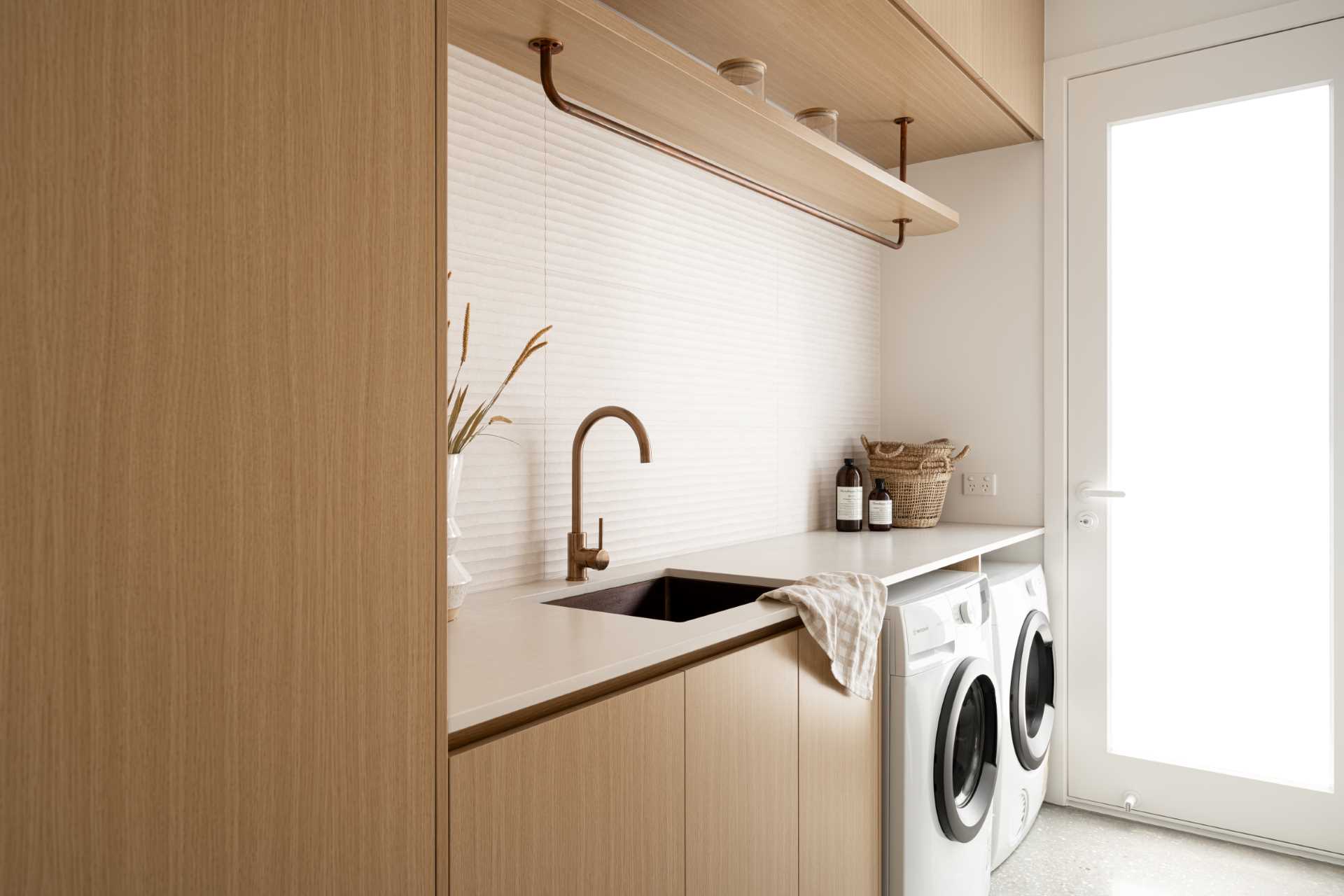 In this contemporary laundry, the countertop travels across the washer and dryer, making the most of the ،e, while the wall adds a textural element.