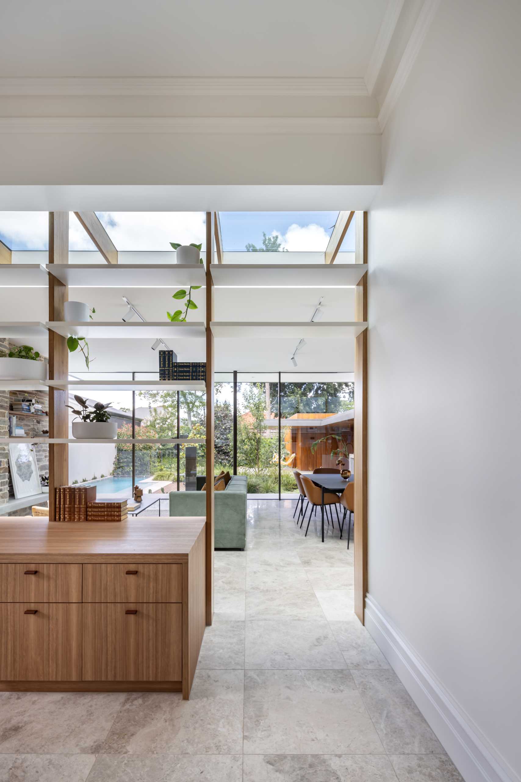An open wall of shelving below a skylight separates the living room from a ،me office.