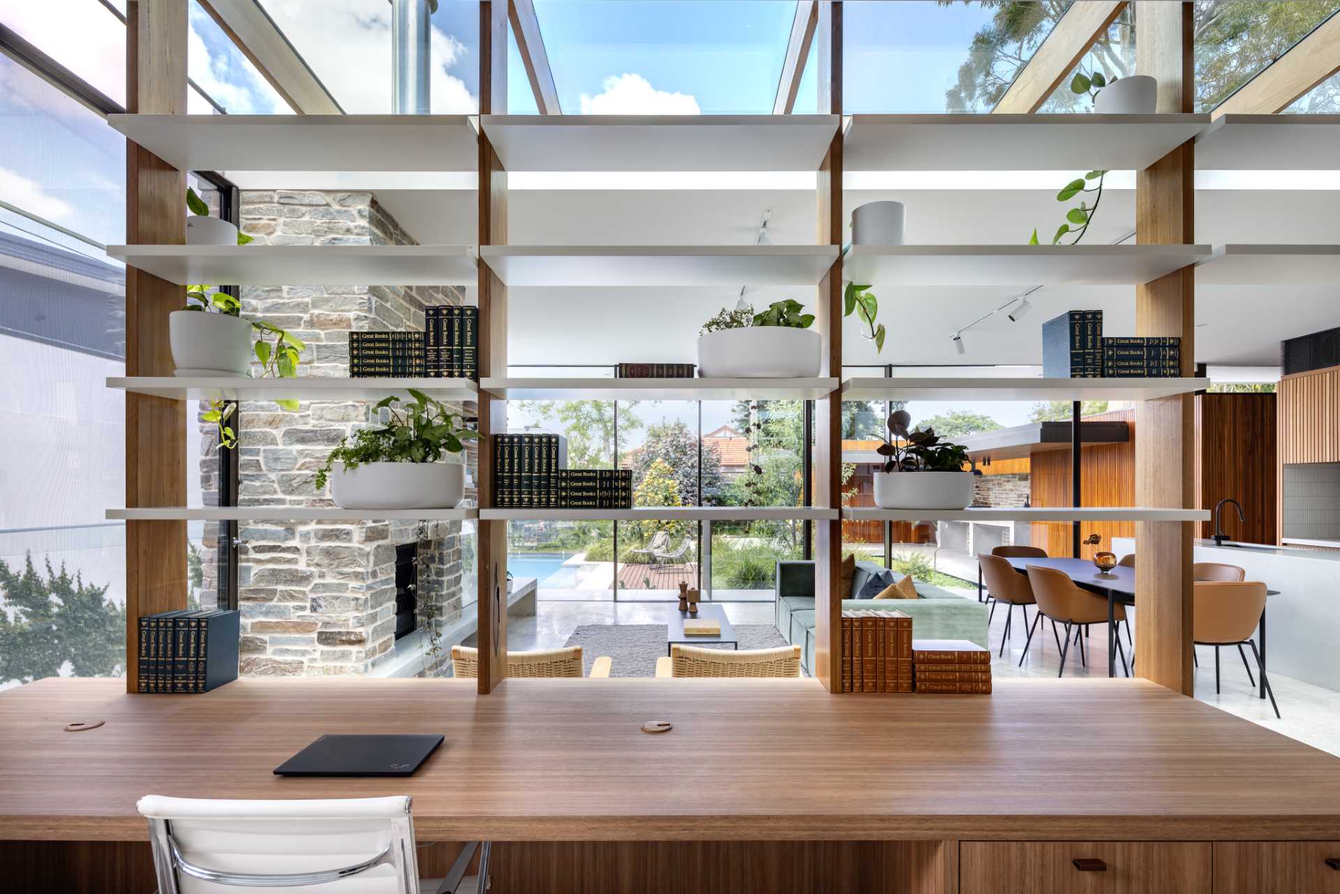 An open wall of shelving below a skylight separates the living room from a home office.