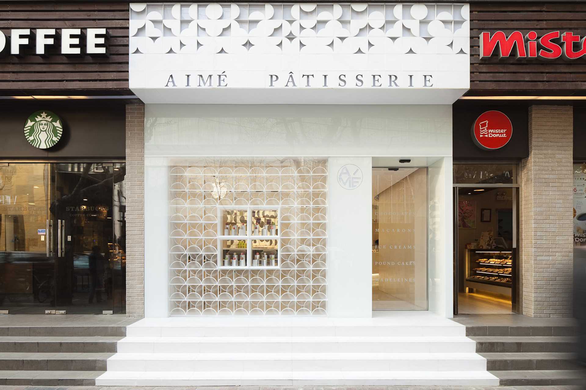 A modern patisserie with a white exterior, whose design is inspired by the act of opening one of the gift boxes that holds their colorful macarons.