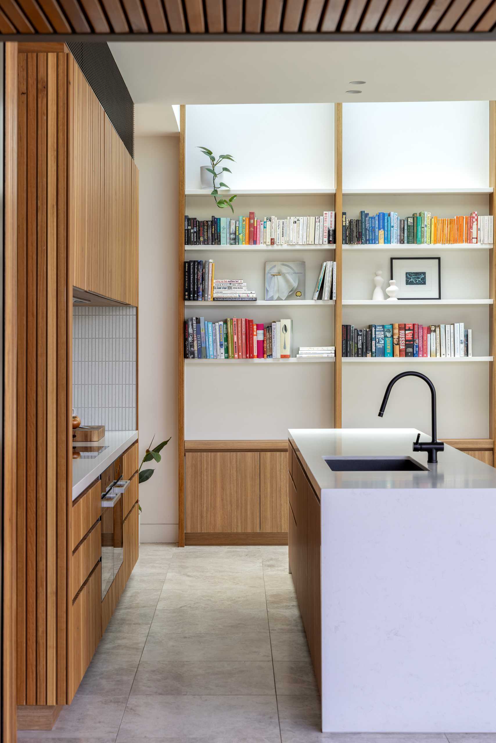 A modern kitchen features wood cabinets, Japanese ceramic tiles, laid vertically as a backsplash, and a minimalist stone island.