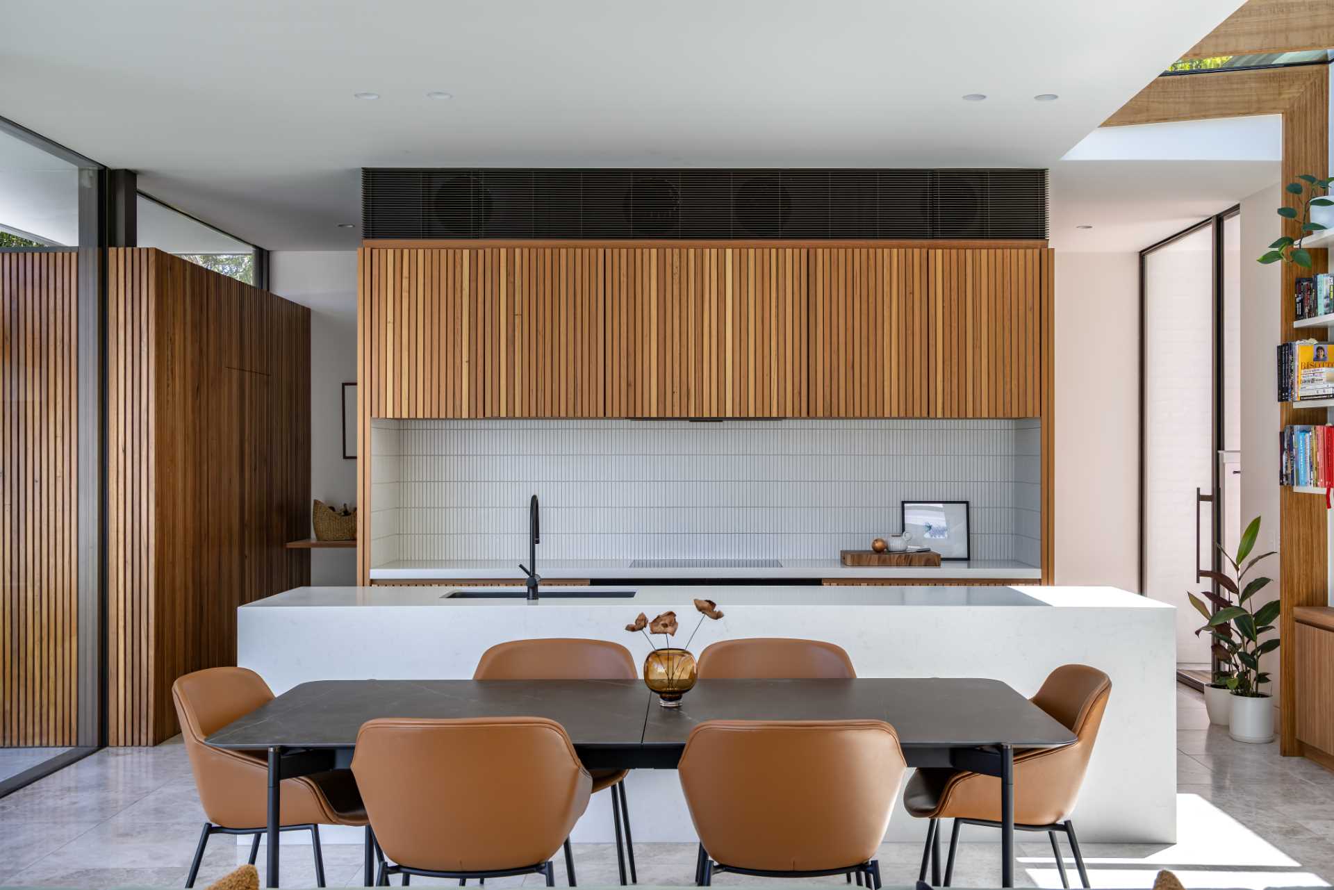 A modern kitchen features wood cabinets, Japanese ceramic tiles, laid vertically as a backsplash, and a minimalist stone island.