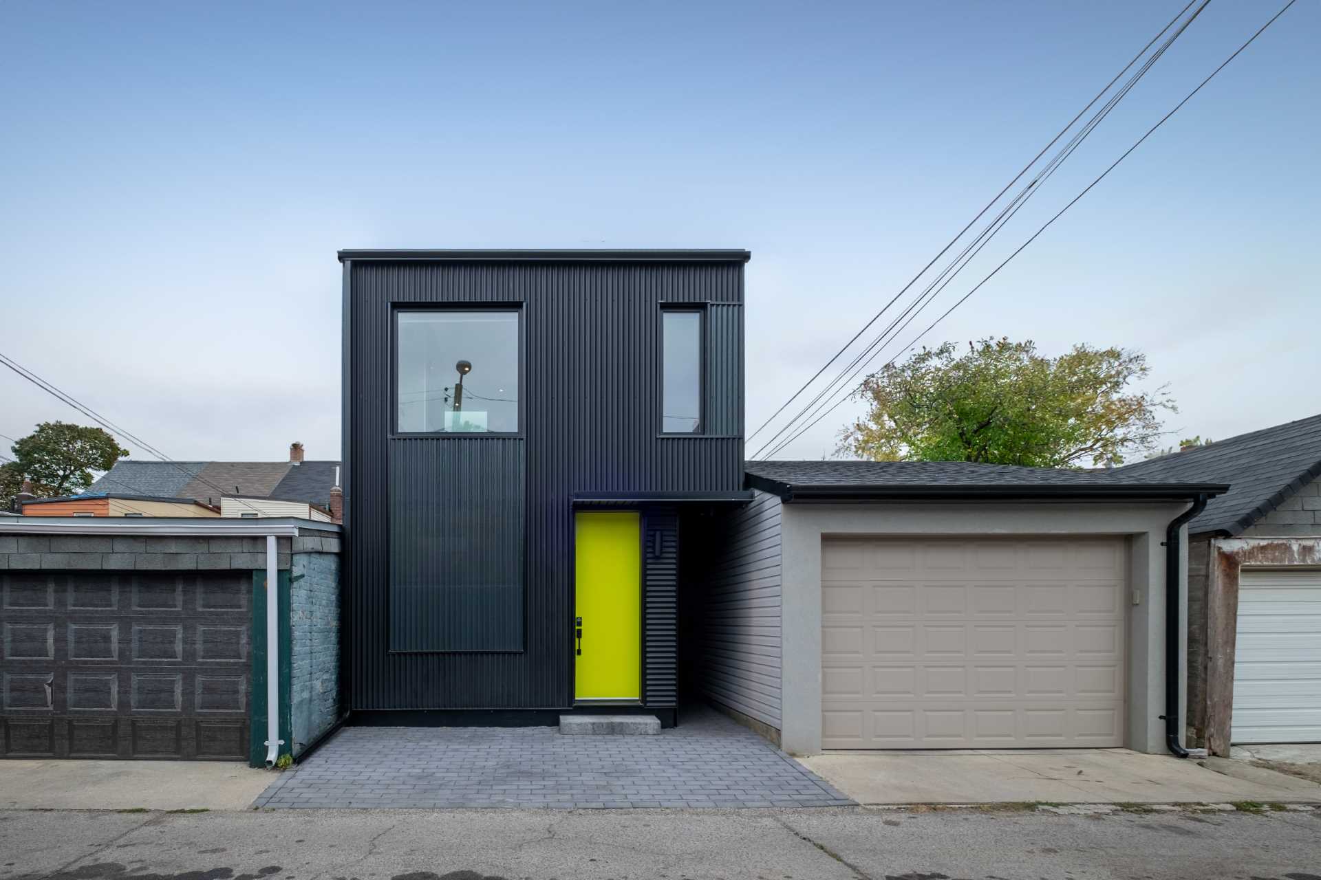 A modern two-storey laneway house with a black exterior and bright yellow door.