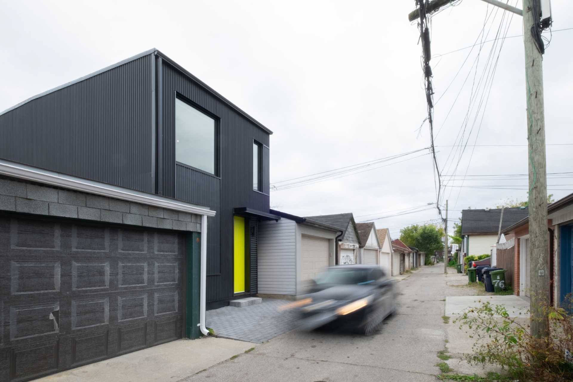 A modern two-storey laneway house with a black exterior and bright yellow door.