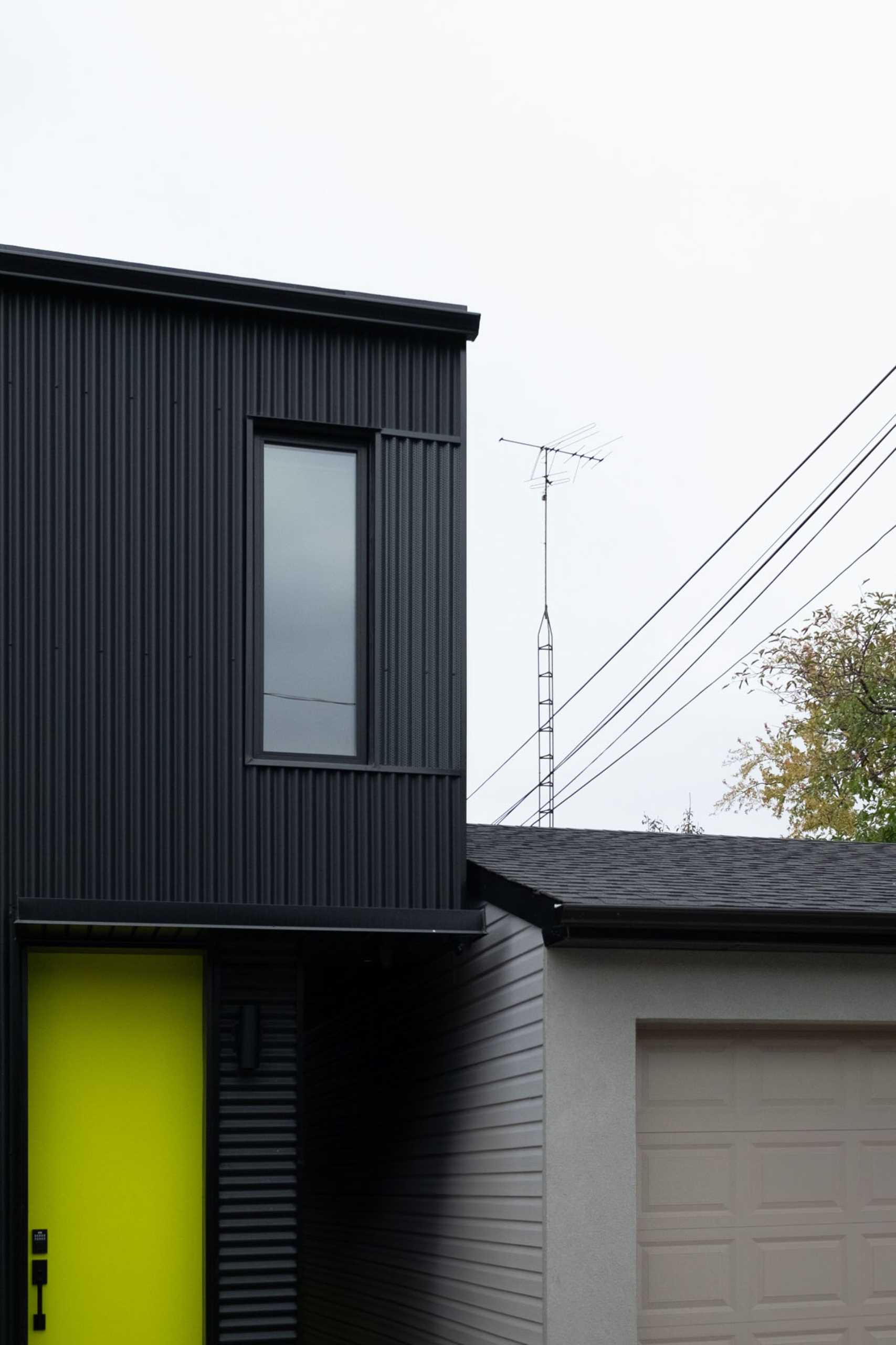 A modern laneway house with a black exterior and bright yellow door.