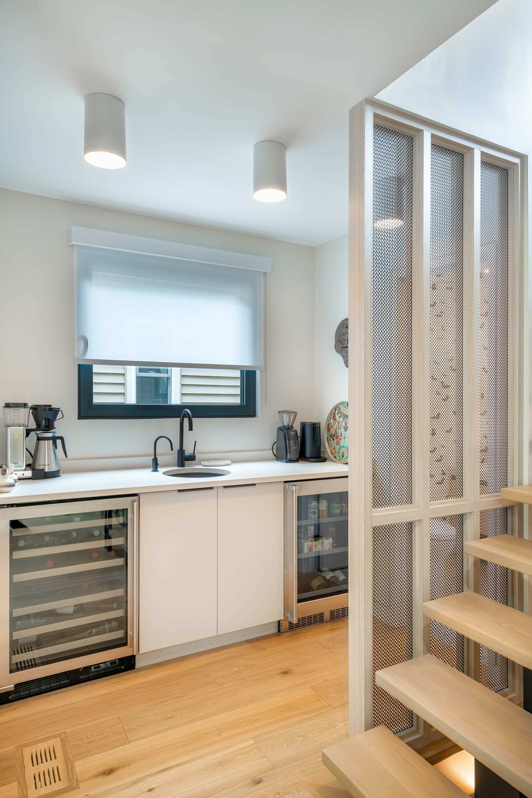 A coffee station features white cabinetry and multiple bar fridges as well as a small sink.