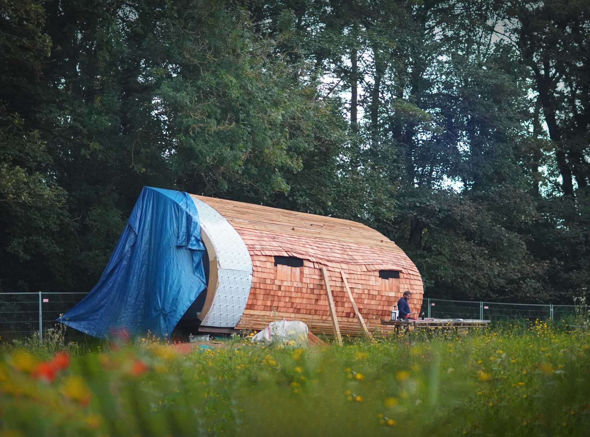 A small organically shaped cabin clad in wood shingles.