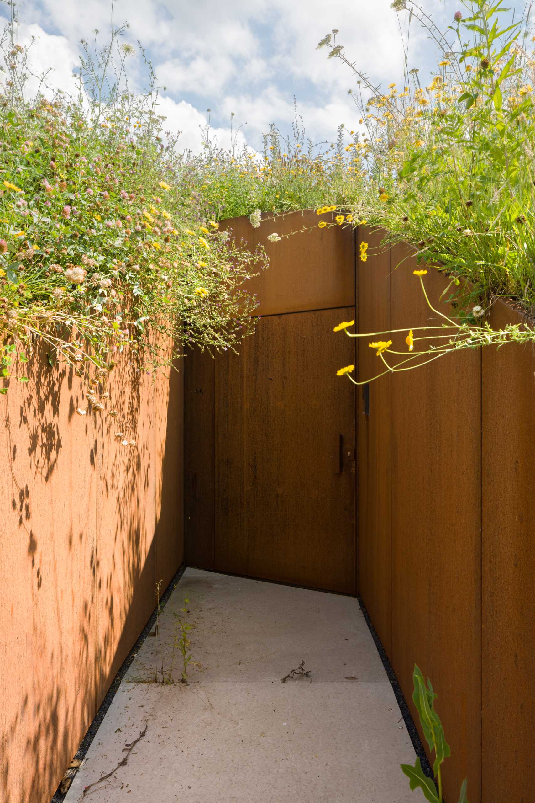 A weathered steel-lined entry between a hillside, that leads to a pivoting door.