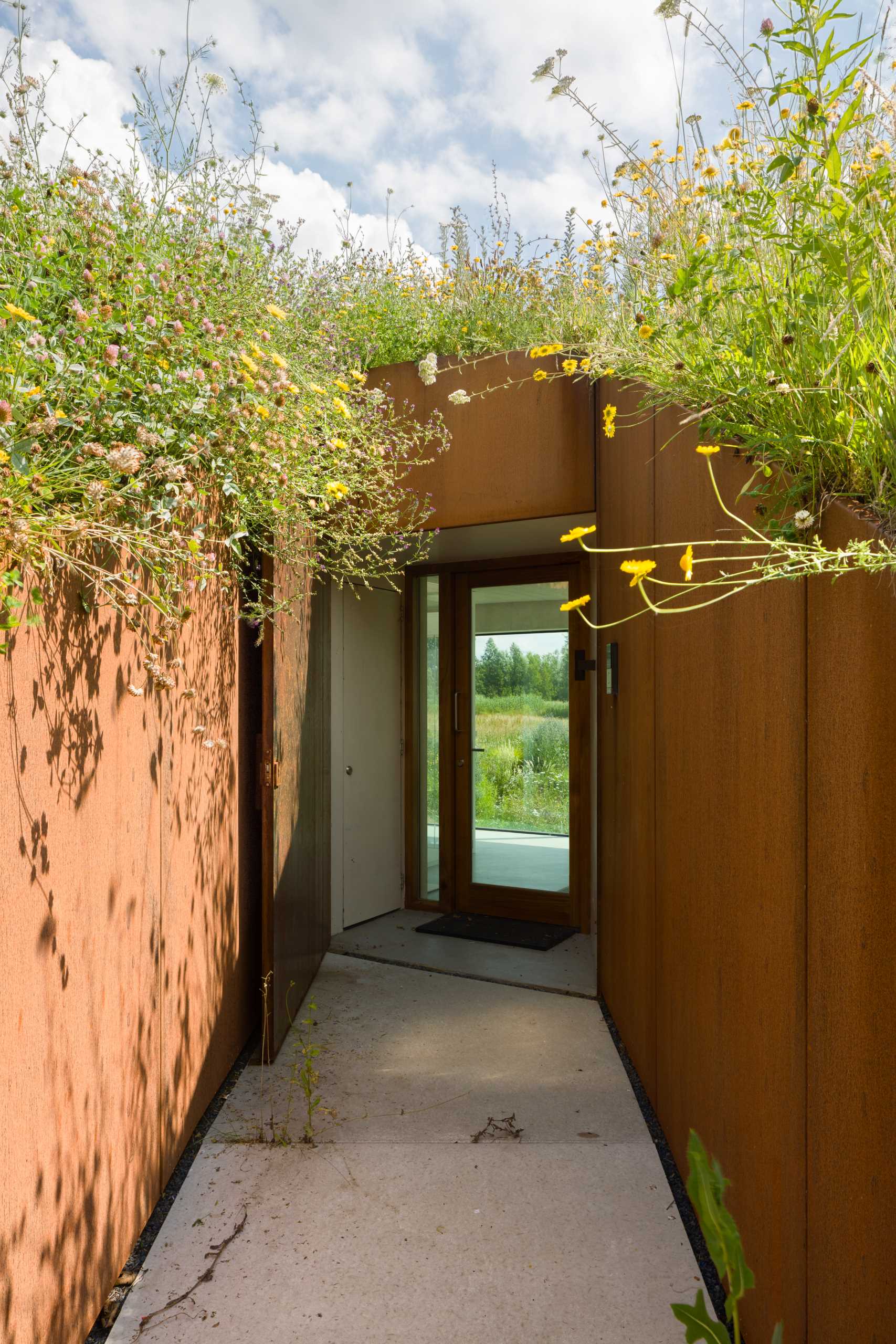 A weathered steel-lined entry between a hillside, that leads to a pivoting door.