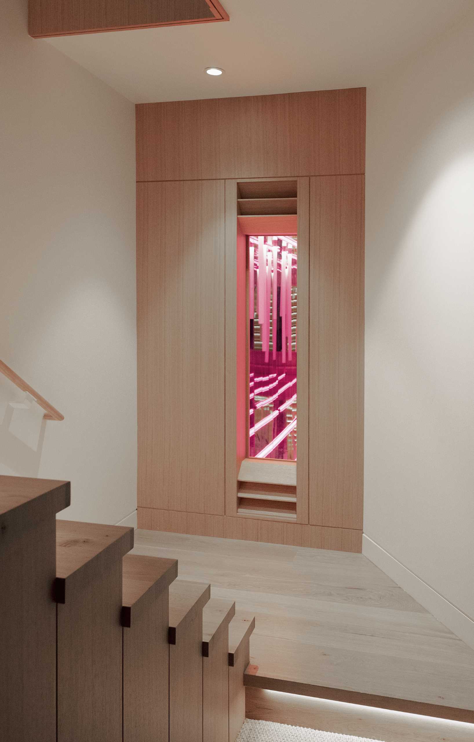 A modern home includes a psychedelic ‘infinity room’ that exists in a foundation quirk. Mirrors, light-tubes, and a wood viewport were used to create a unique lighting installation.