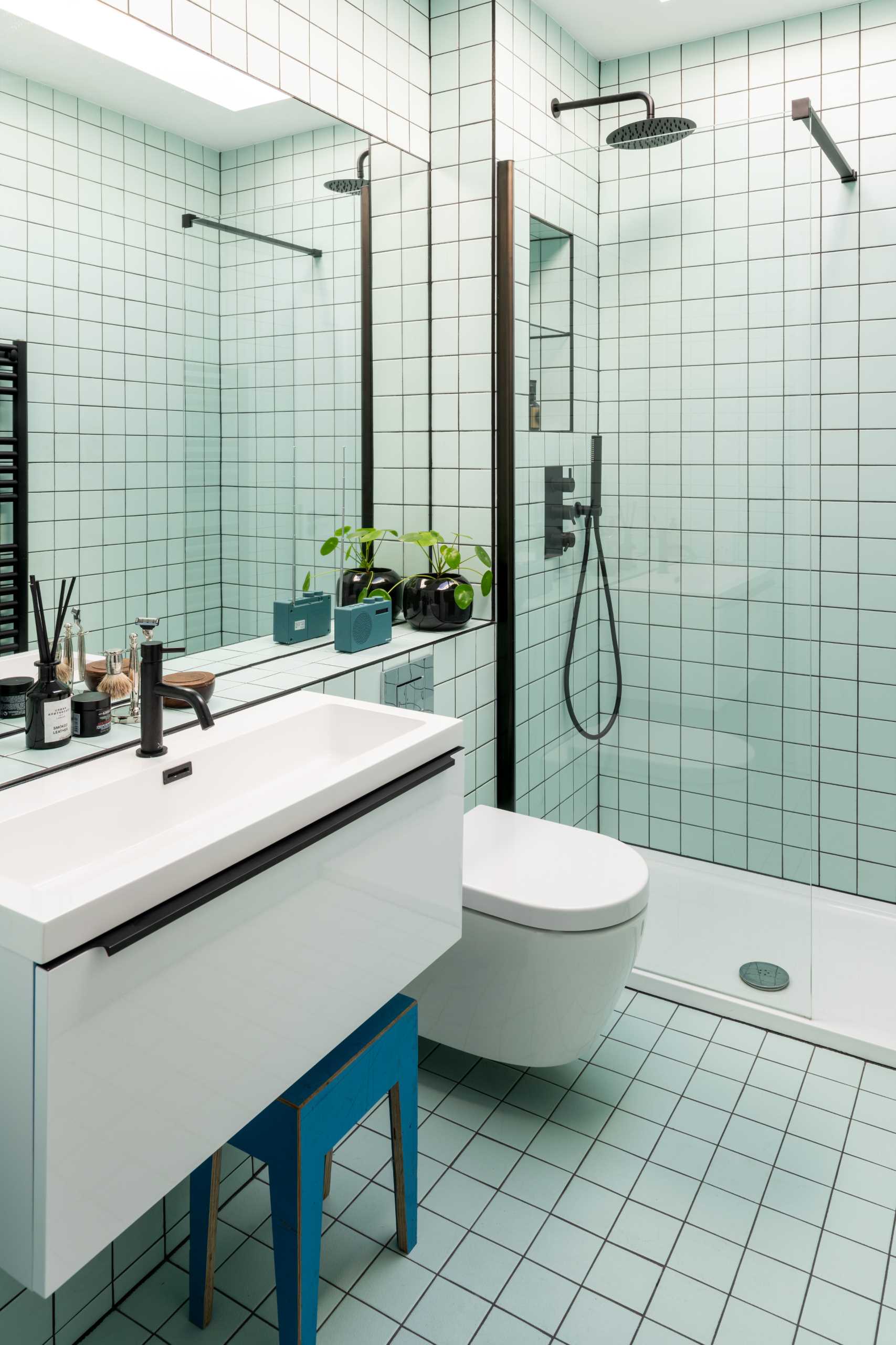 In a bathroom, square tiles cover the walls and floor, while black accents provide a contrasting element.