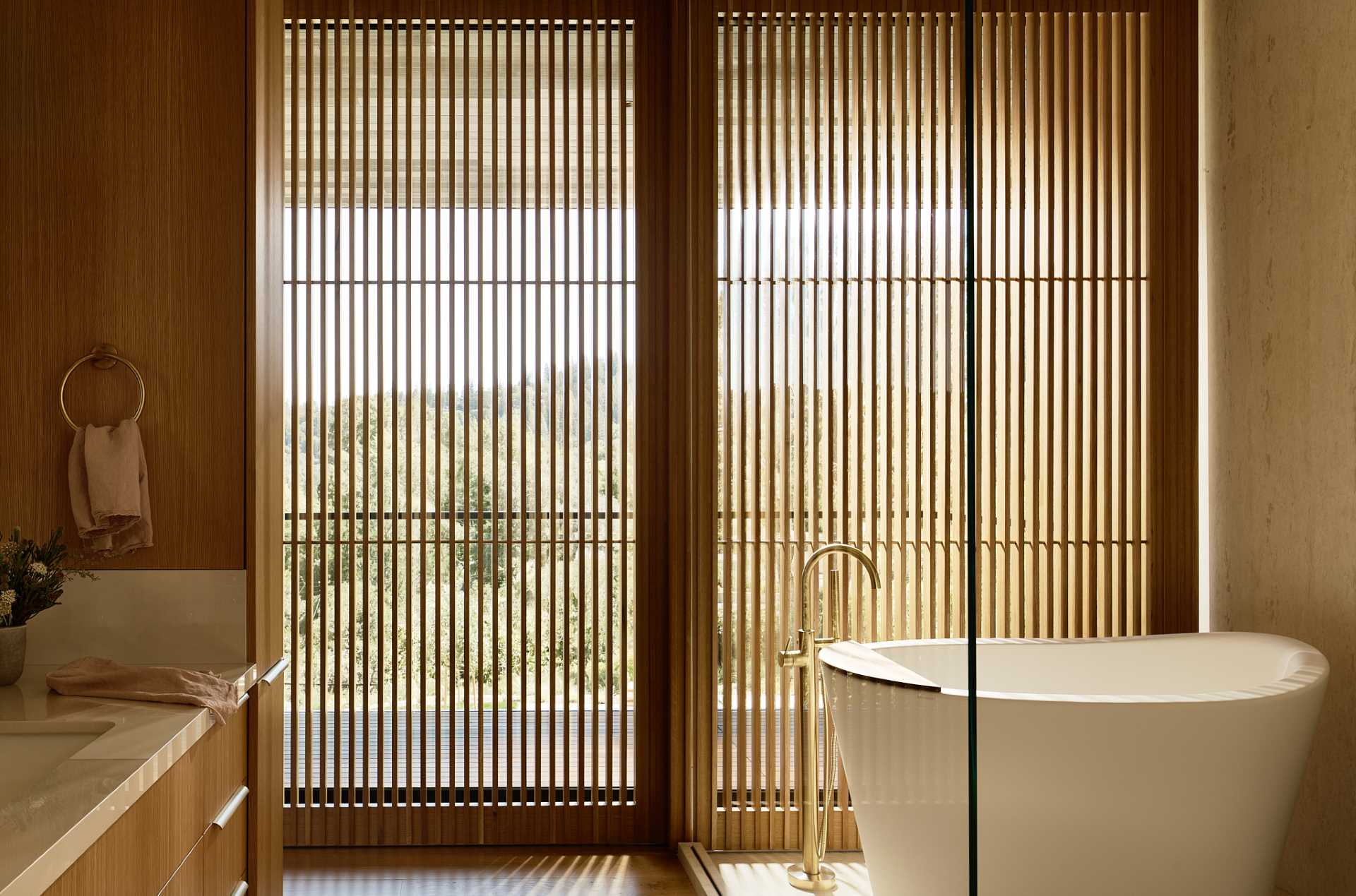 In this bathroom, a freestanding bathtub is positioned in front of the windows, while wood slats provide privacy.
