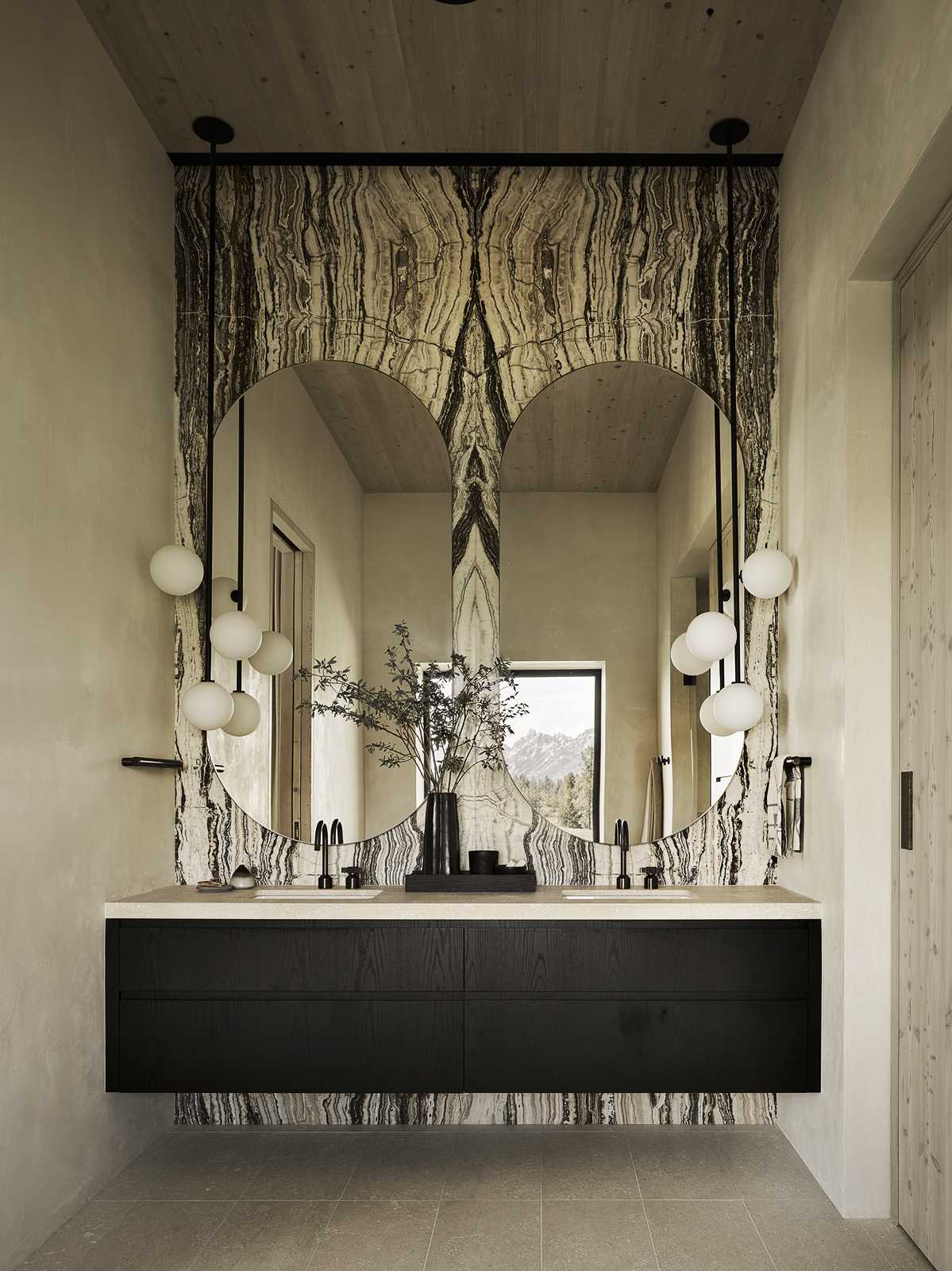 A contemporary bathroom with rounded mirrors and a stone accent wall.