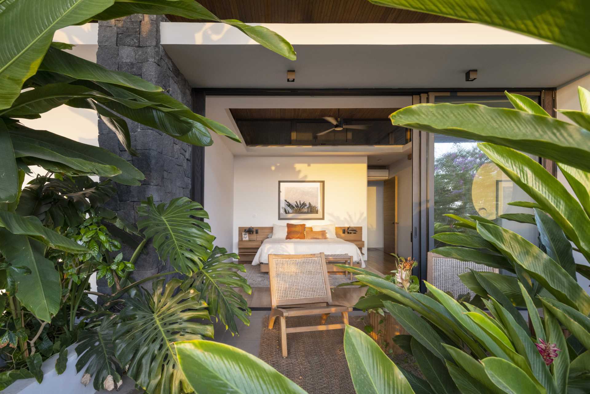 A bedroom with a sliding door opens to a private patio filled with plants.