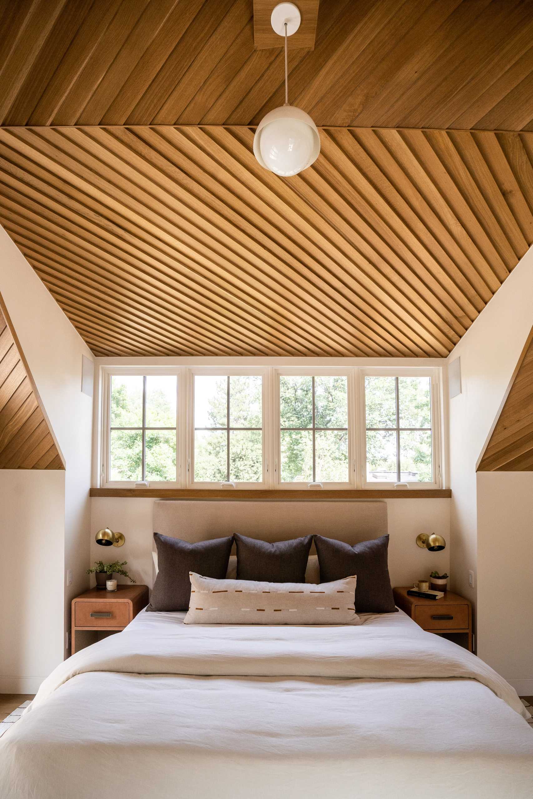 In this main bedroom, the ceiling is composed of lap siding installed at an angle, aligned perfectly at the ridge, while built-in dressers make smart use of the available ،e.