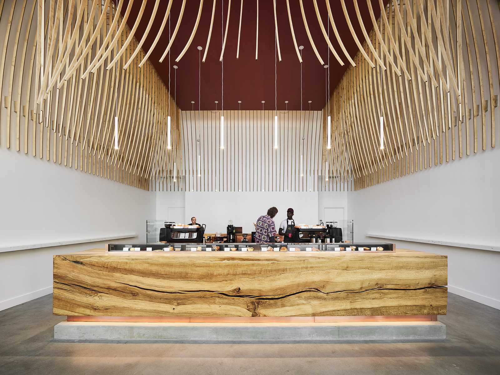 A modern coffee bar with a large wood bar and a sculptural element made from 272 wood slats.