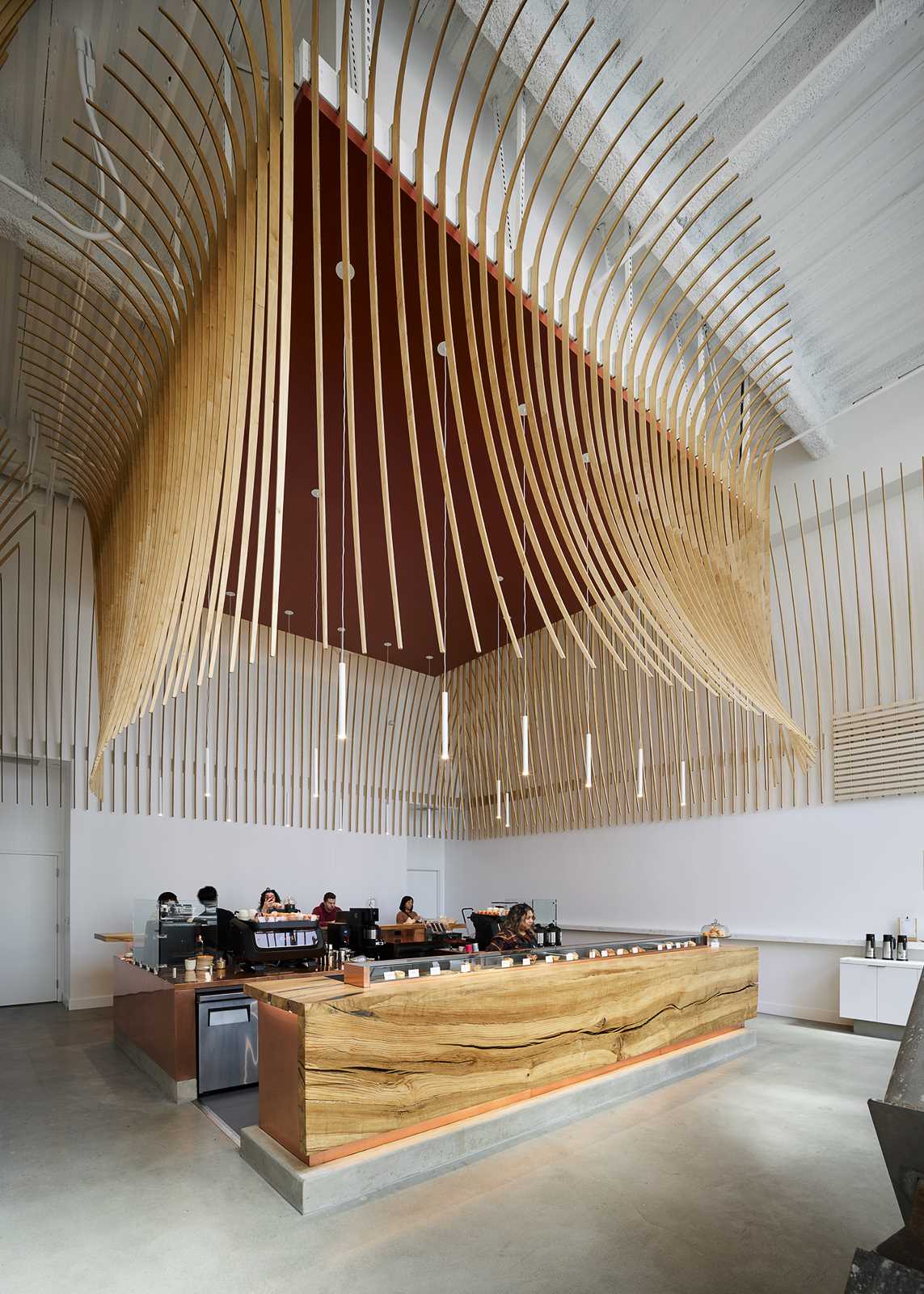 A modern coffee bar with a large wood bar and a sculptural element made from 272 wood slats.