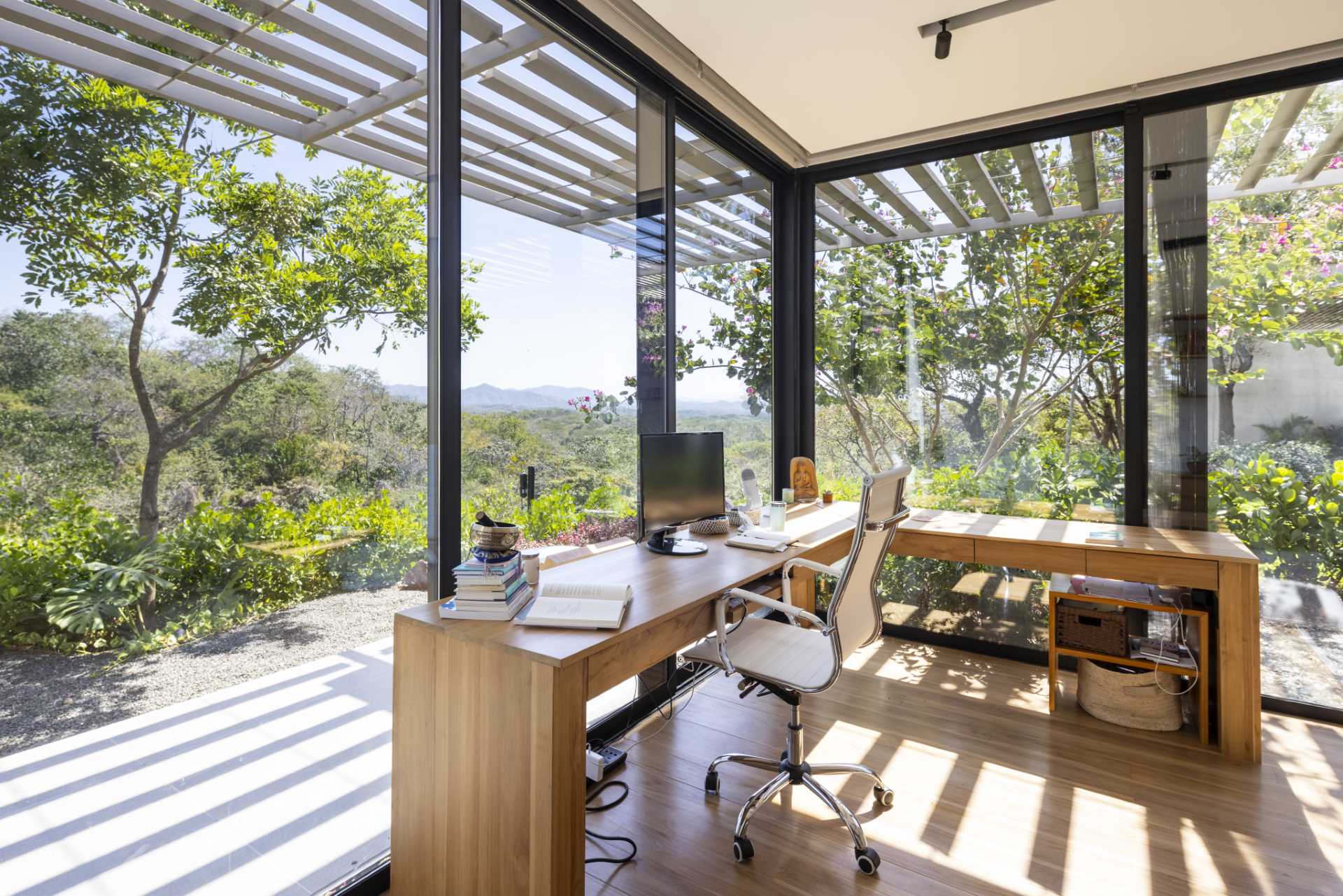 In a home office, a desk is positioned in front of floor-to-ceiling black-framed windows with views of the landscape.