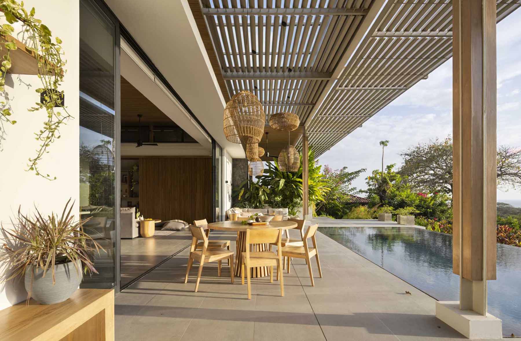 The pergola, which has oversized pendant lights and fans hanging above seating and dining areas, connects with the living room inside, and the swimming pool with views of the ocean.