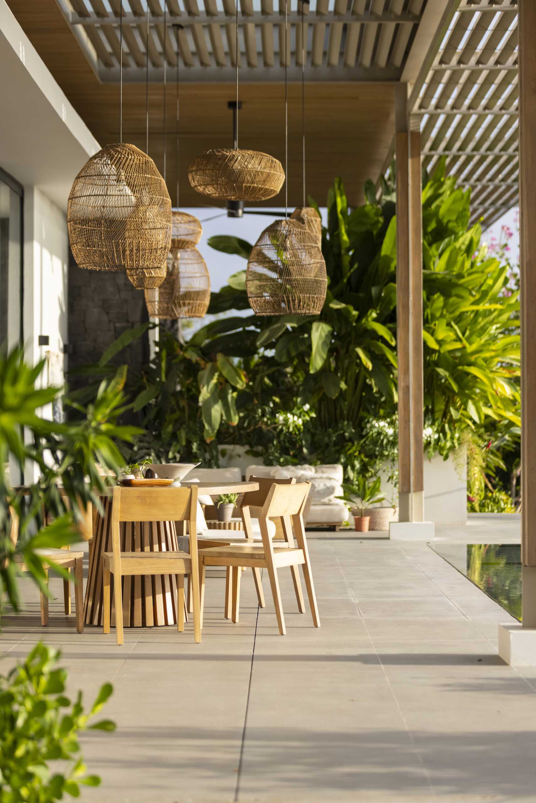 The pergola, which has oversized pendant lights and fans hanging above seating and dining areas, connects with the living room inside, and the swimming pool with views of the ocean.