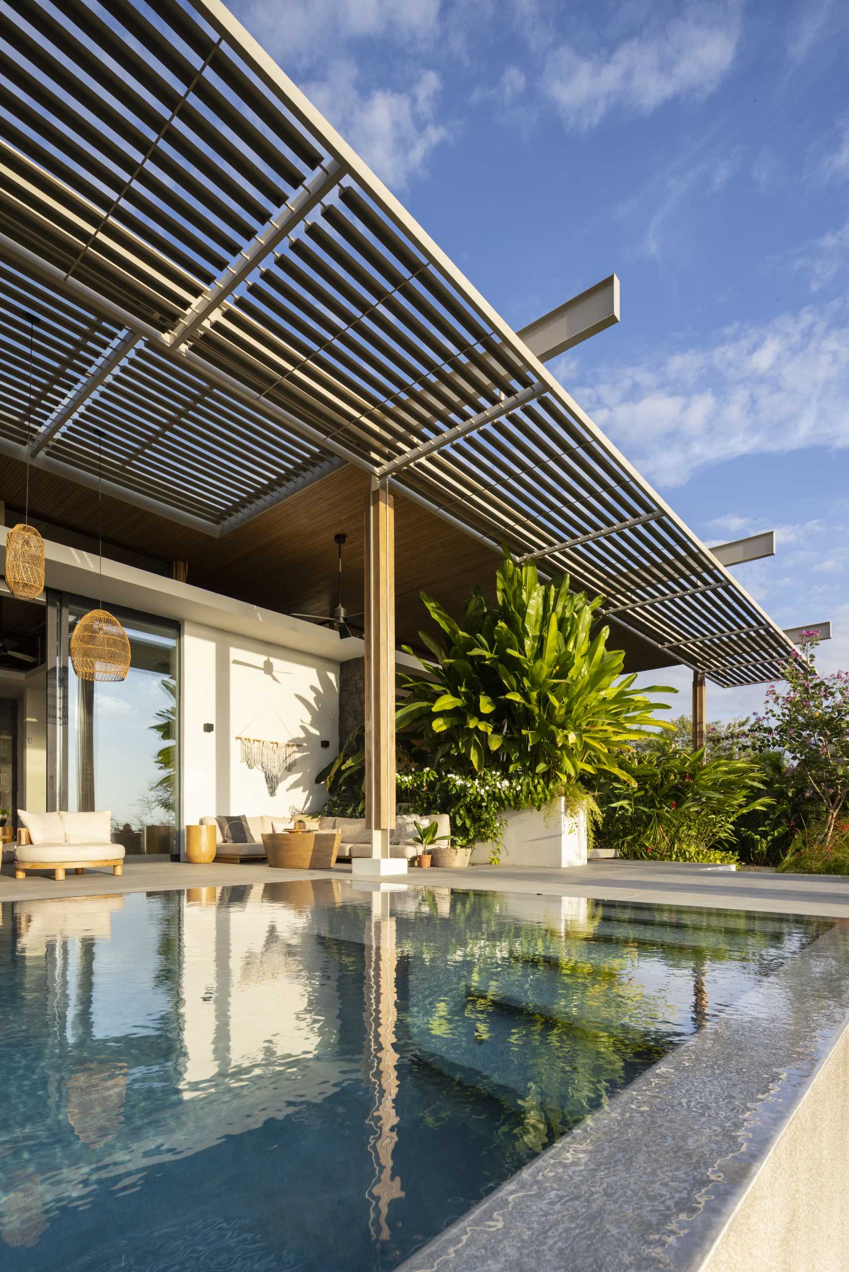 The pergola, which has oversized pendant lights and fans hanging above seating and dining areas, connects with the living room inside, and the swimming pool with views of the ocean.