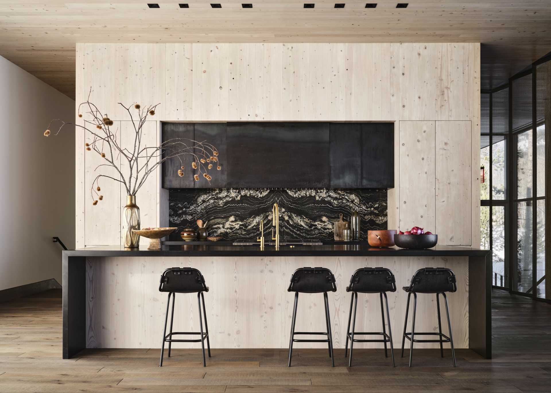 In the kitchen, minimalist light wood cabinets contrast the large island, backsplash, and range،od.