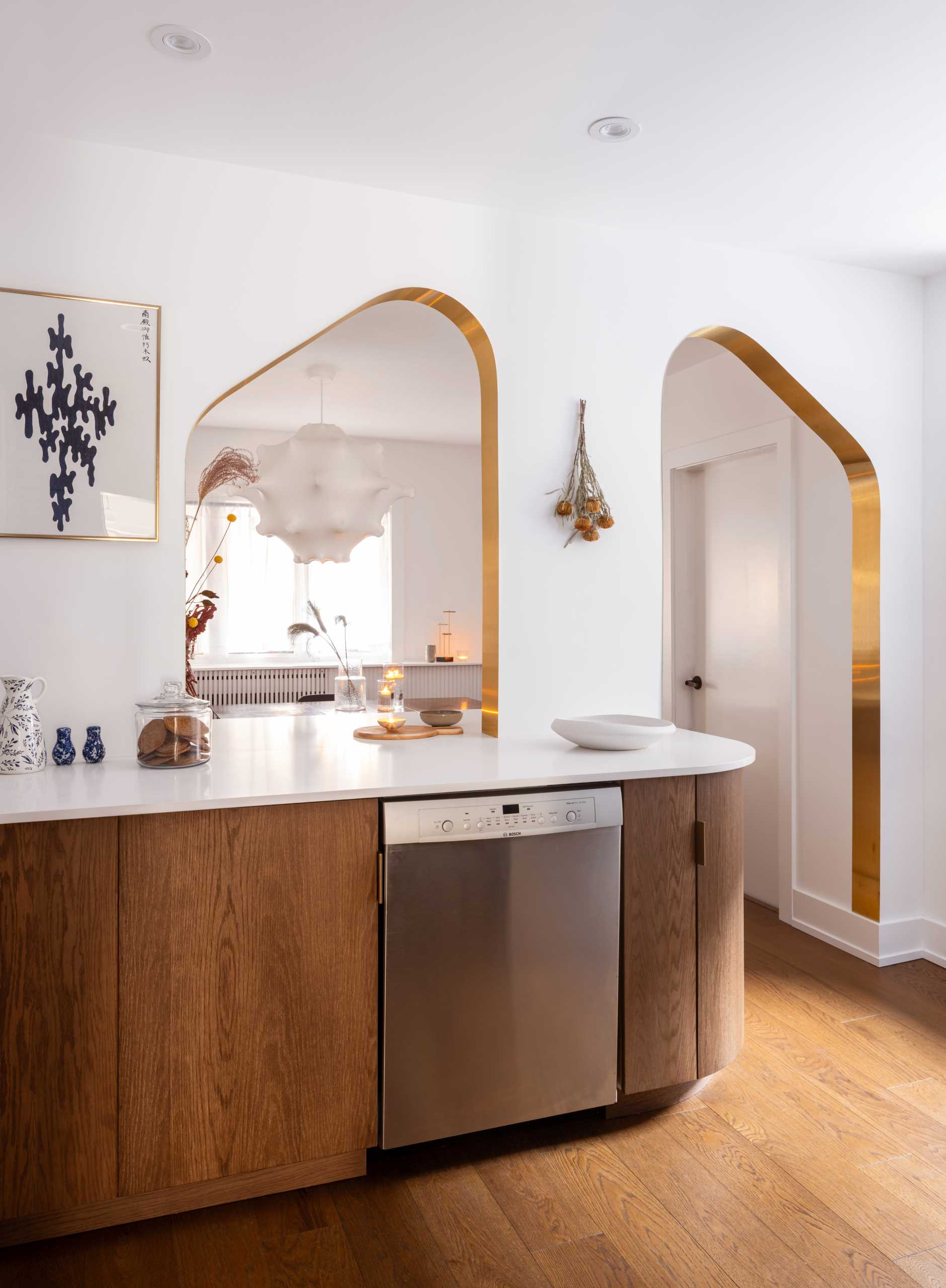 A modern kitchen with dark wood and white cabinets, white countertops, Dutch “Delft” tile, and brass-lined arches.
