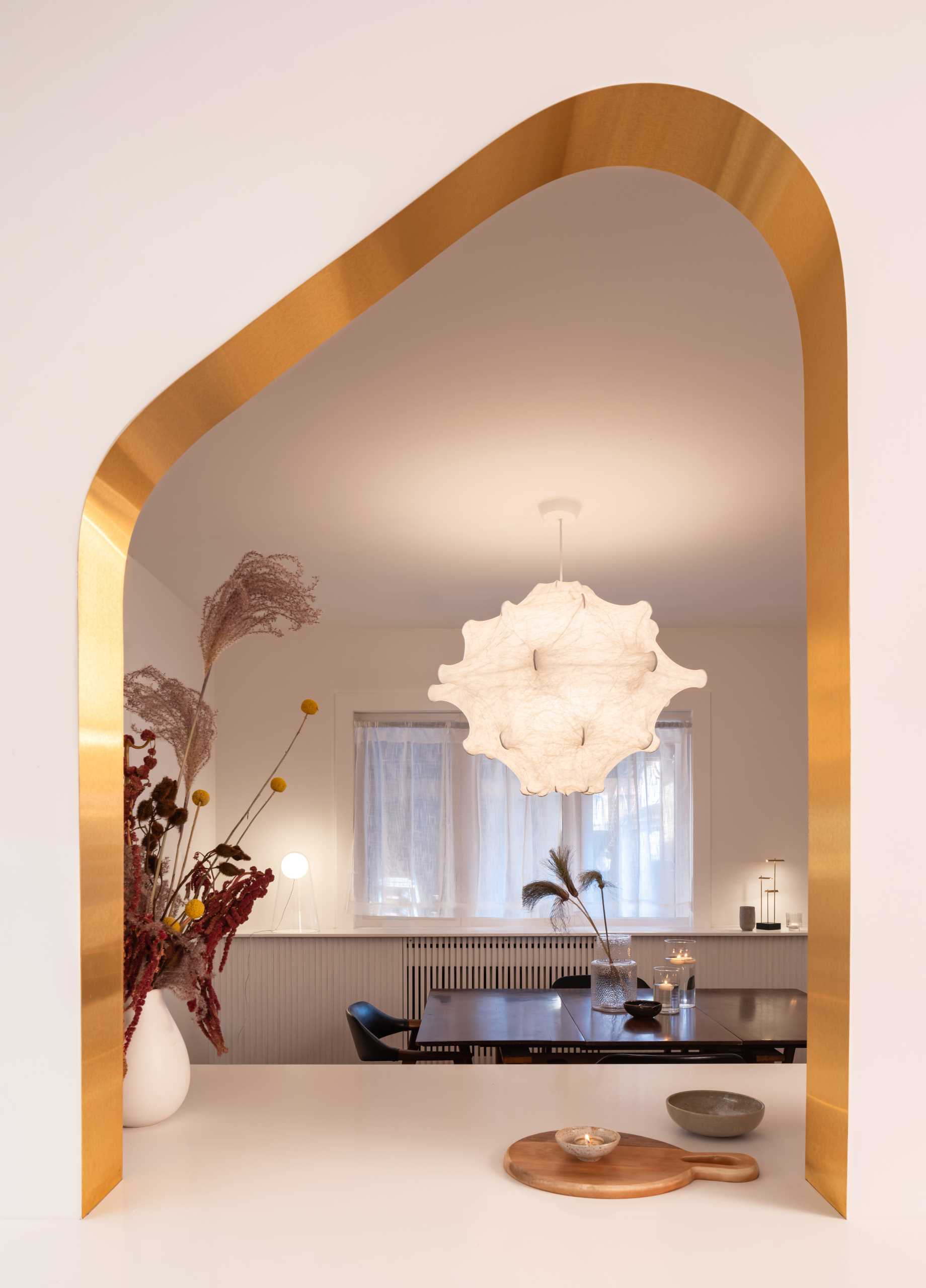 A modern kitchen with dark wood and white cabinets, white countertops, Dutch “Delft” tile, and brass-lined arches.