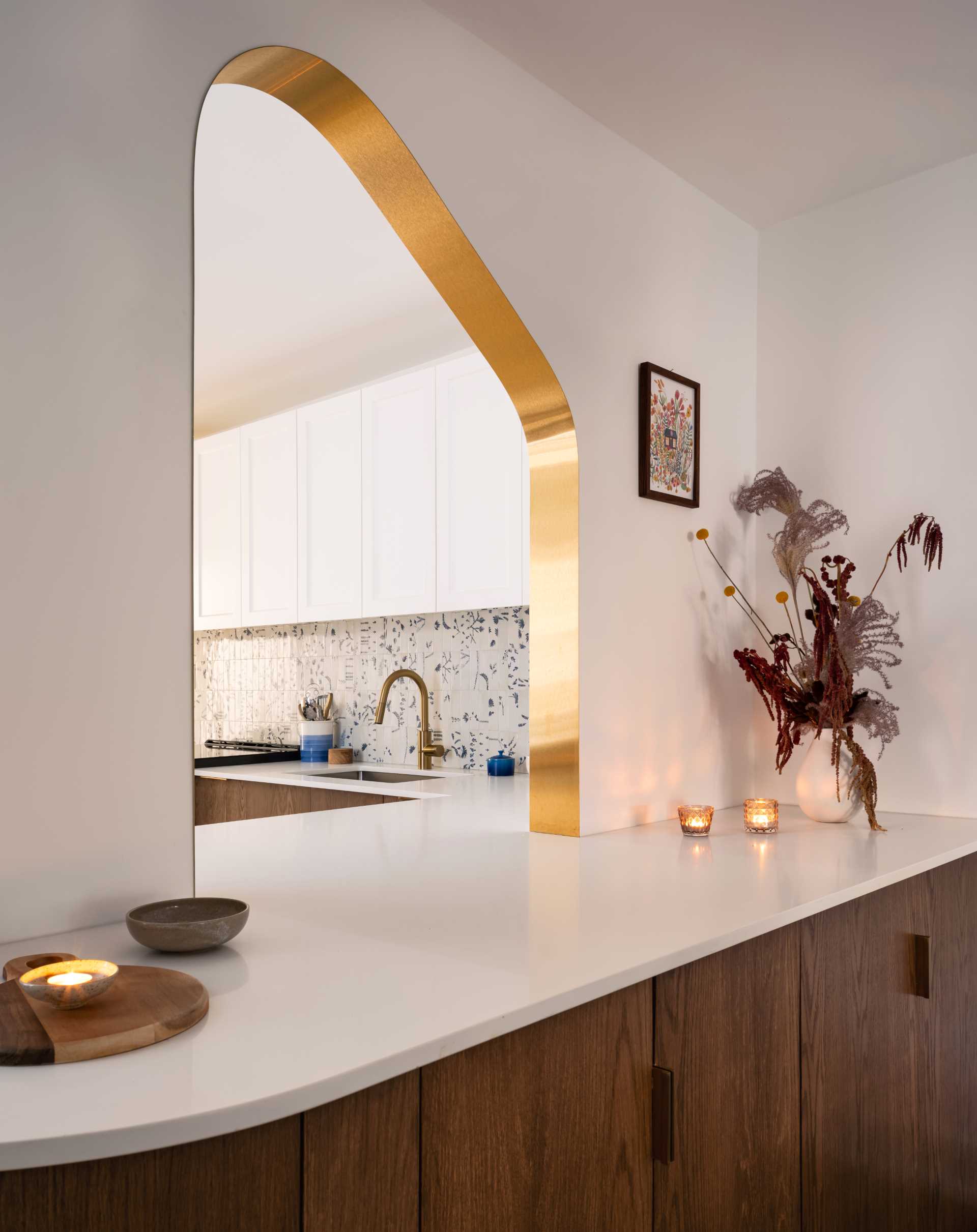 A modern kitchen with dark wood and white cabinets, white countertops, Dutch “Delft” tile, and brass-lined arches.