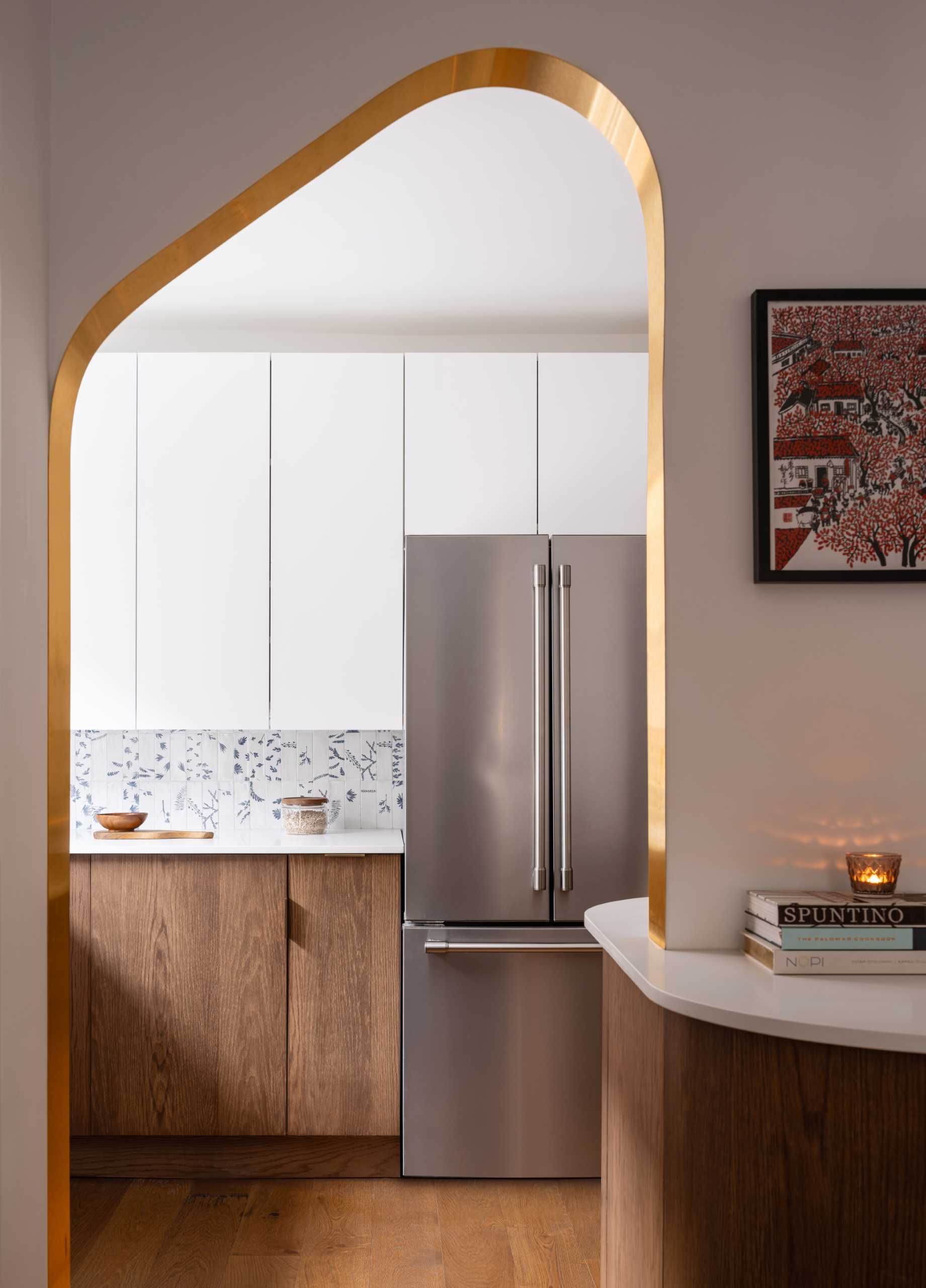 A modern kitchen with dark wood and white cabinets, white countertops, Dutch “Delft” tile, and brass-lined arches.